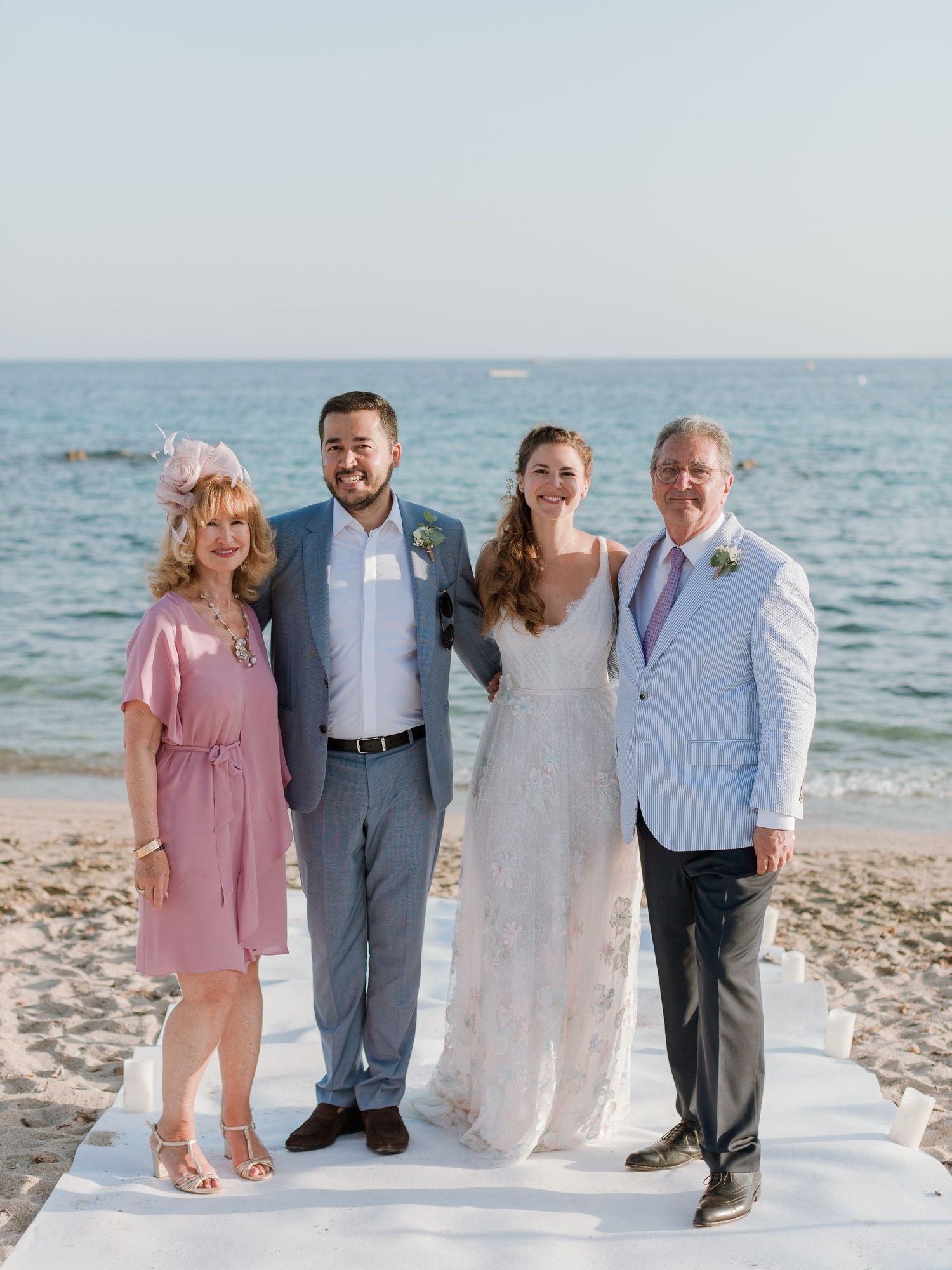 Quatre personnes posant ensemble lors d'une cérémonie de mariage sur la plage ; la mariée porte une robe blanche en dentelle et le marié