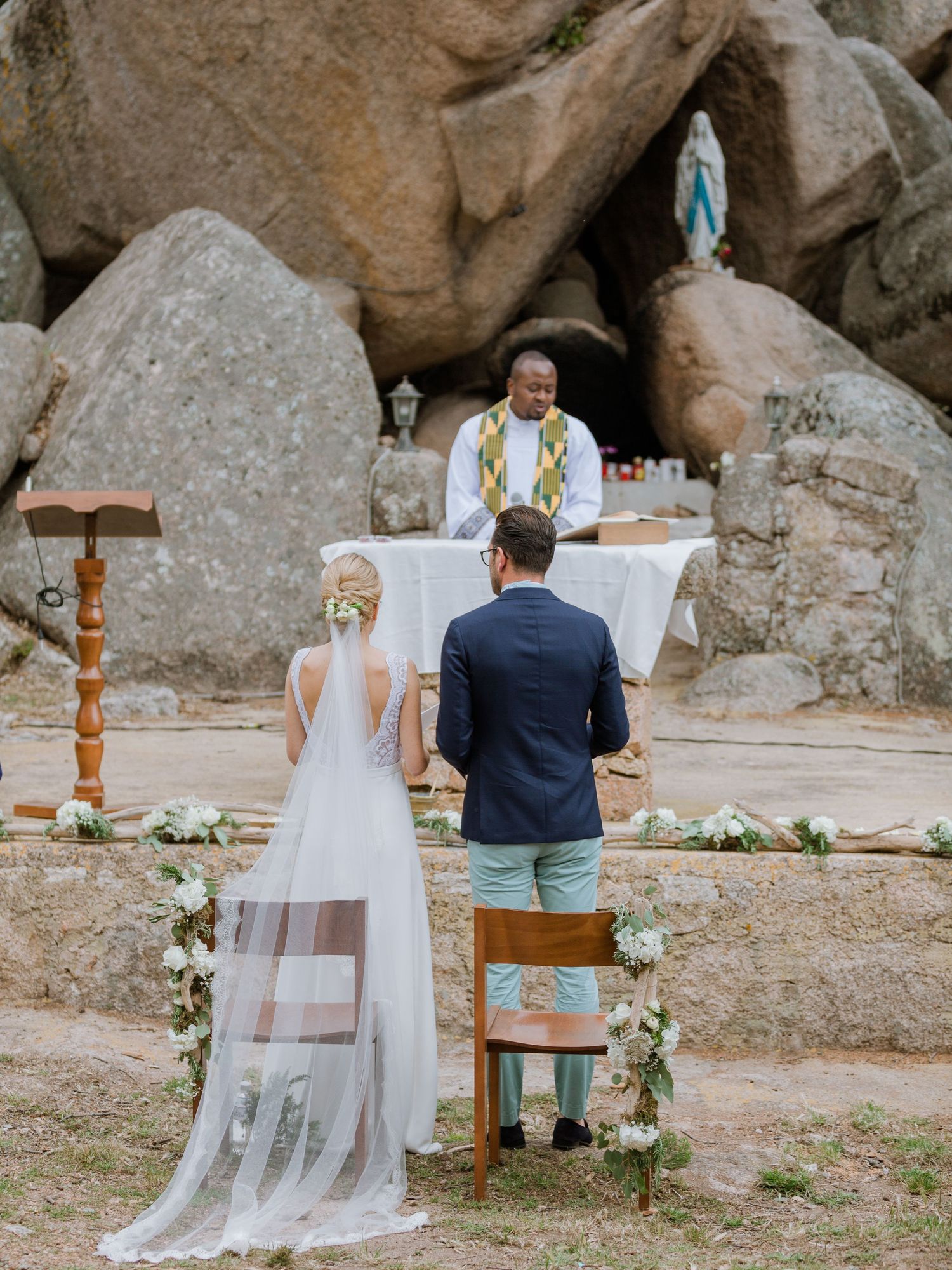 Cérémonie de mariage en plein air dans une grotte rocheuse, avec les mariés et l'officiant autour d'un autel décoré de fleurs.