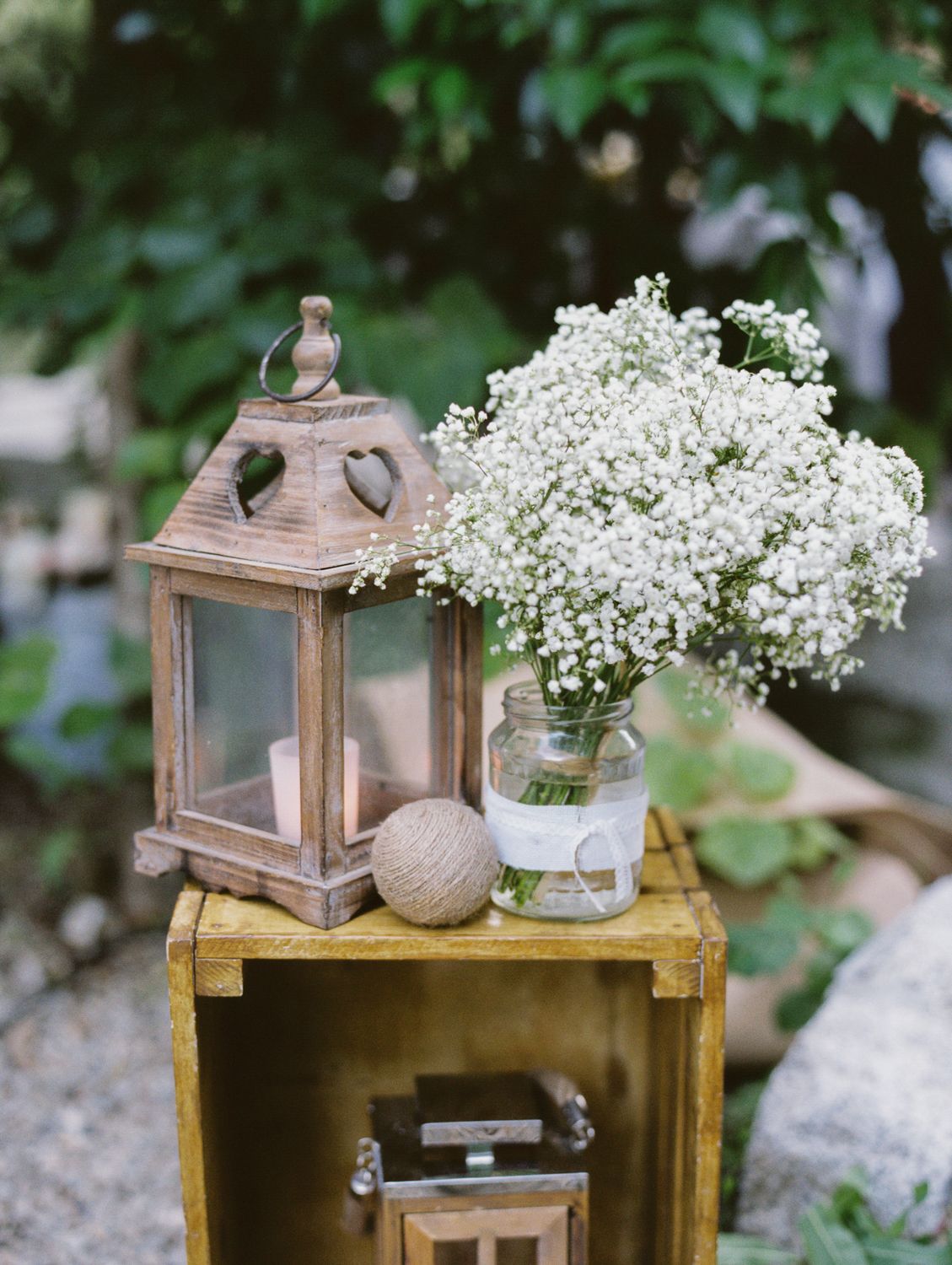 Rustic wooden lantern with candle beside baby's breath flowers in mason jar on vintage yellow crate for wedding decor.
