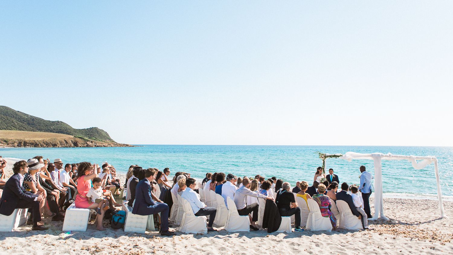 Cérémonie de mariage en plein air sur la plage, avec les invités assis sur des chaises blanches face à la mer à Ajaccio