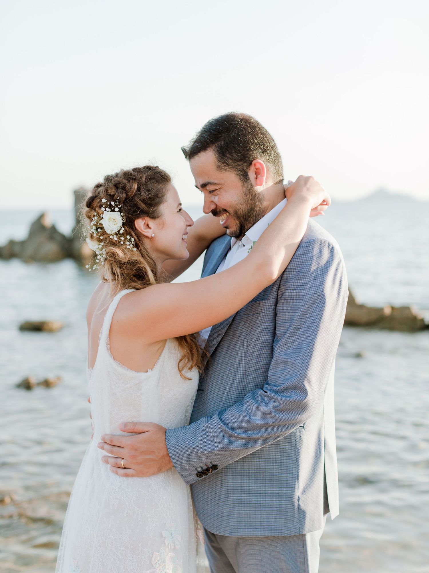 Les mariés s'enlacent tendrement au bord de l'océan et se sourient le jour de leur mariage.