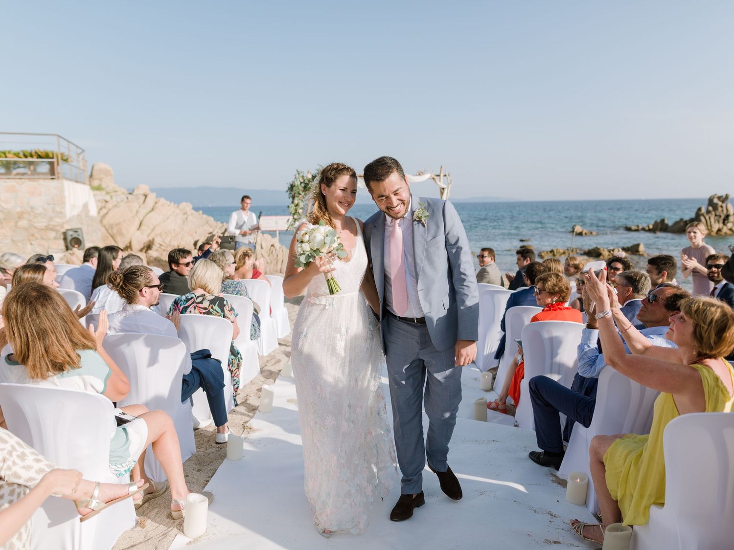 Les mariés remontent l'allée lors d'une magnifique cérémonie de mariage en plein air sur la plage, sous les acclamations des invités.