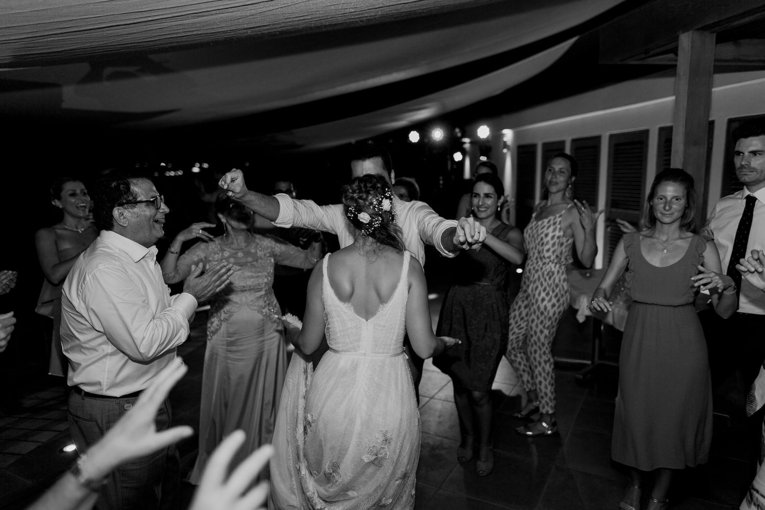 Photo en noir et blanc de la mariée et du marié dansant avec des invités lors d'une réception de mariage animée.