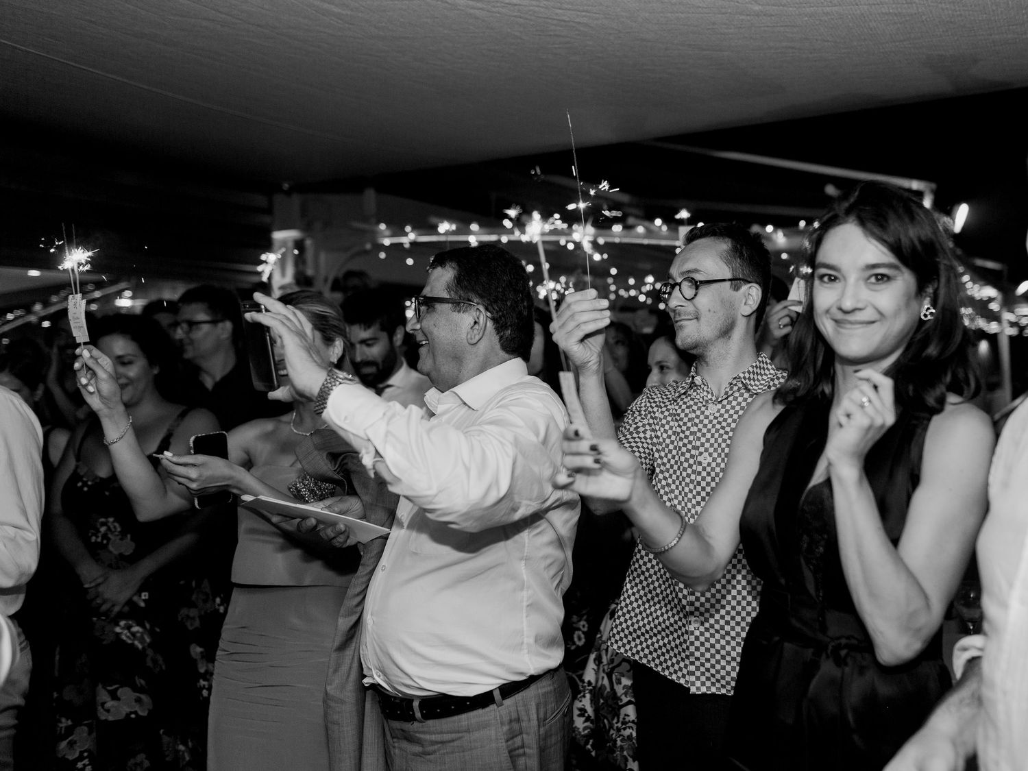 Photo en noir et blanc d'invités tenant des cierges magiques et faisant la fête lors d'une soirée festive.