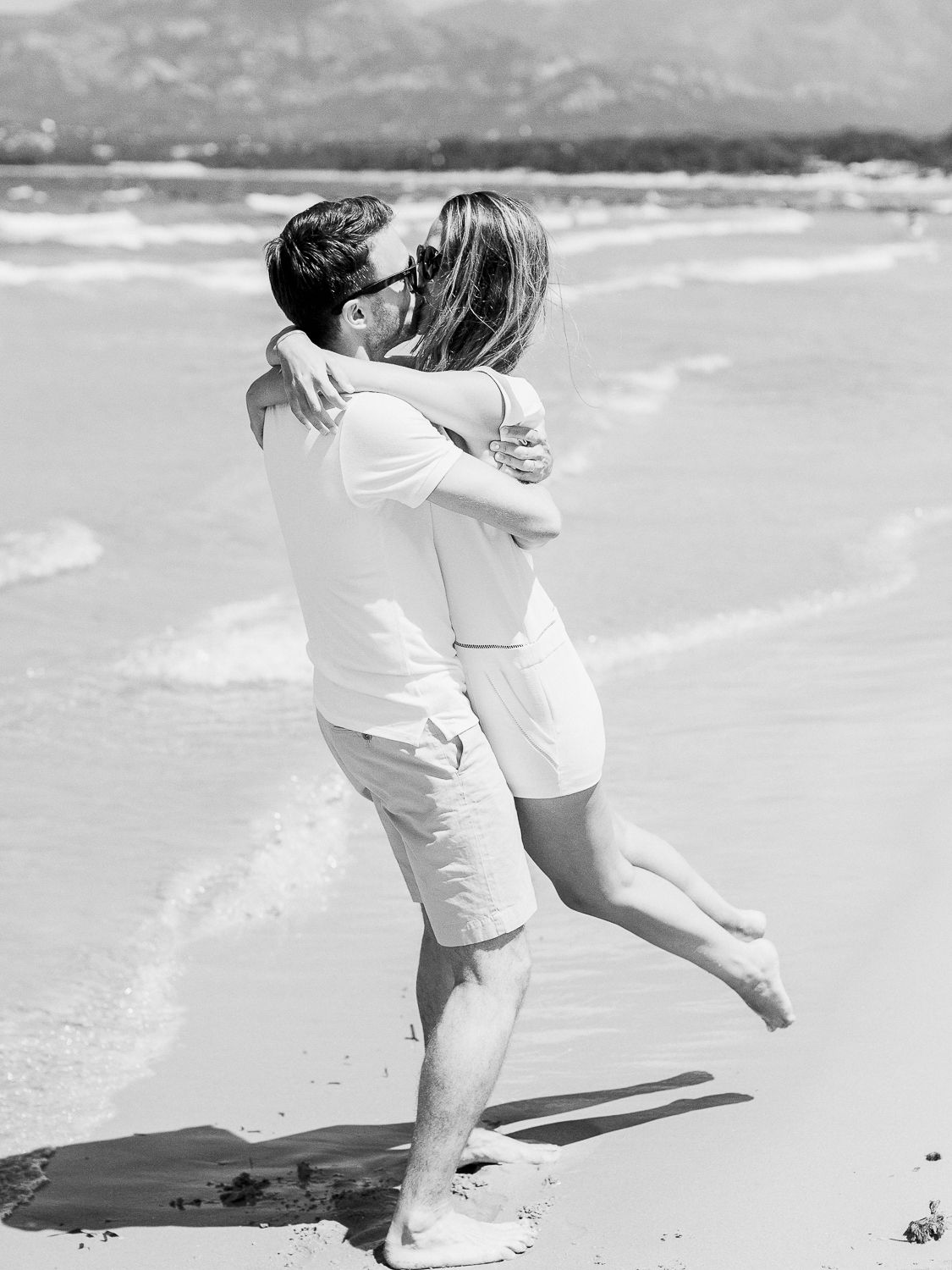 Un couple s'embrasse sur une plage ensoleillée, bercé par les vagues, dans cette photo romantique en noir et blanc à calvi.