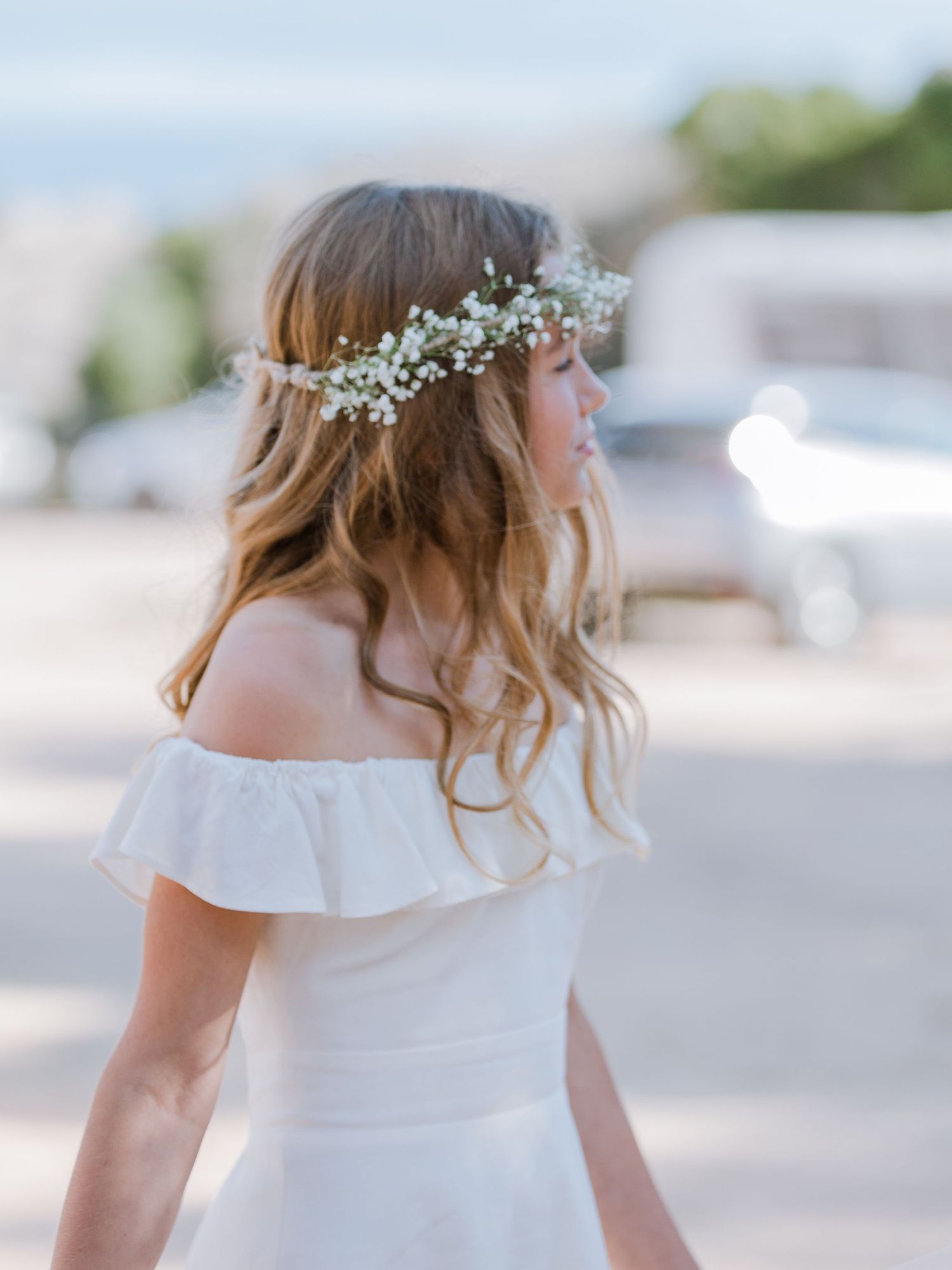 Jeune fille en robe blanche à épaules dénudées portant une couronne de gypsophile, vue de dos.