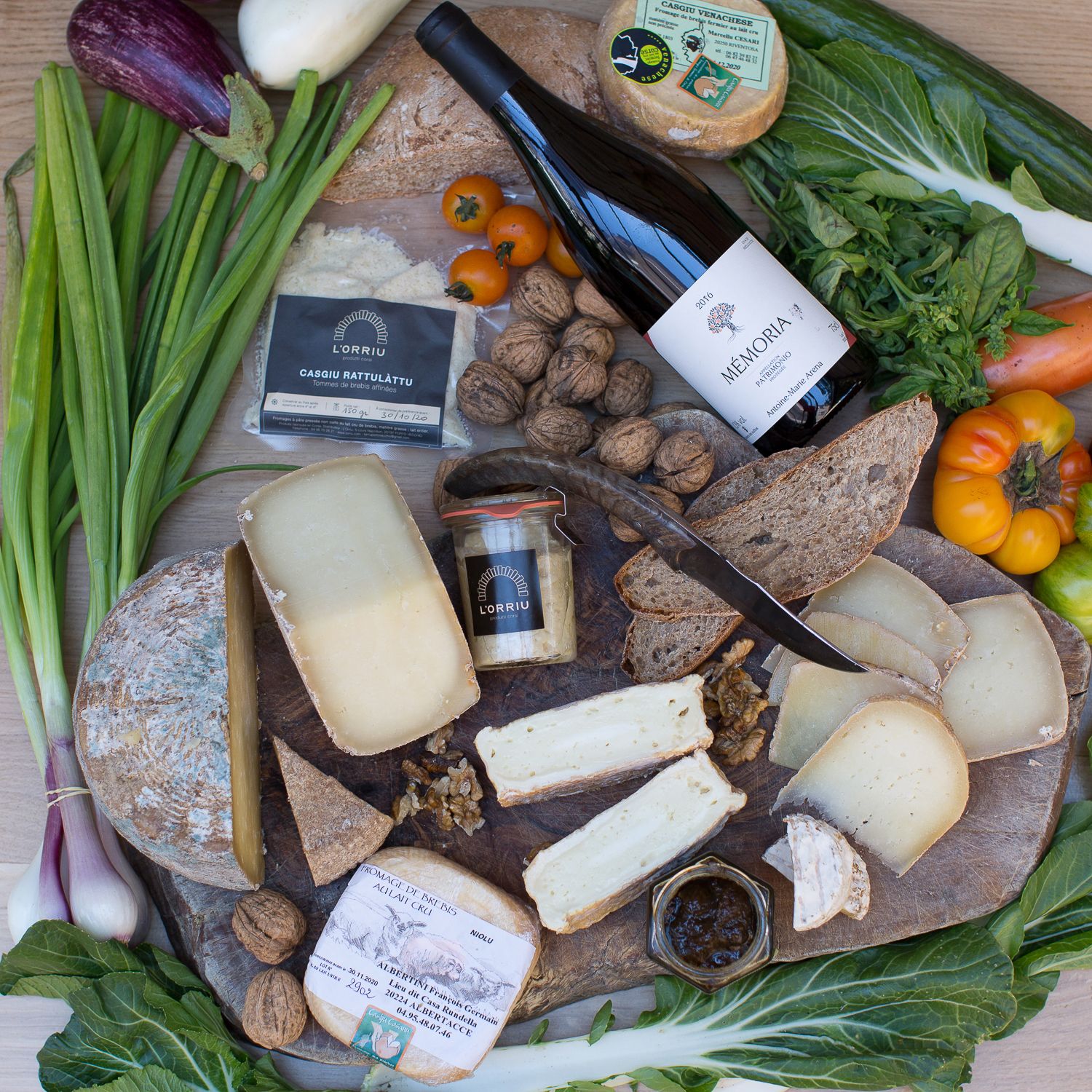 Plateau de fromages artisanaux avec noix, tomates anciennes, pain, vin et légumes frais sur un plateau en bois.