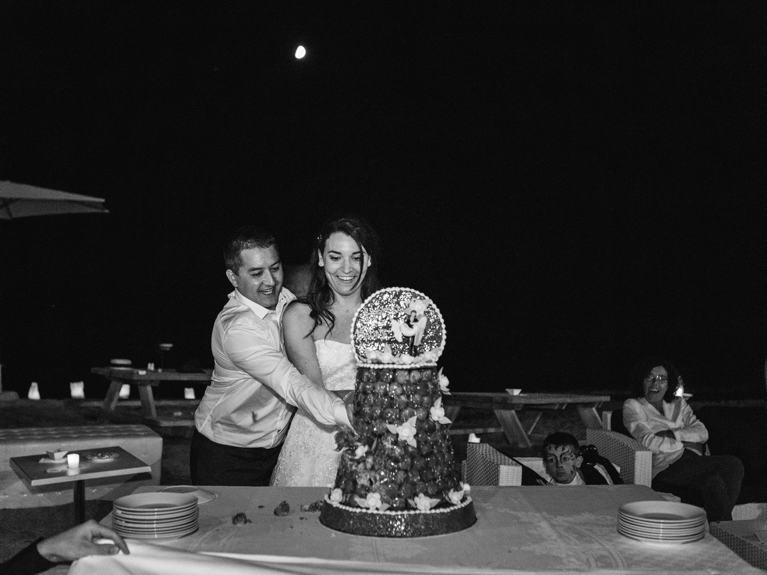Un couple coupant son gâteau de mariage en extérieur, de nuit (photo en noir et blanc). A Capo di Feno à Ajaccio