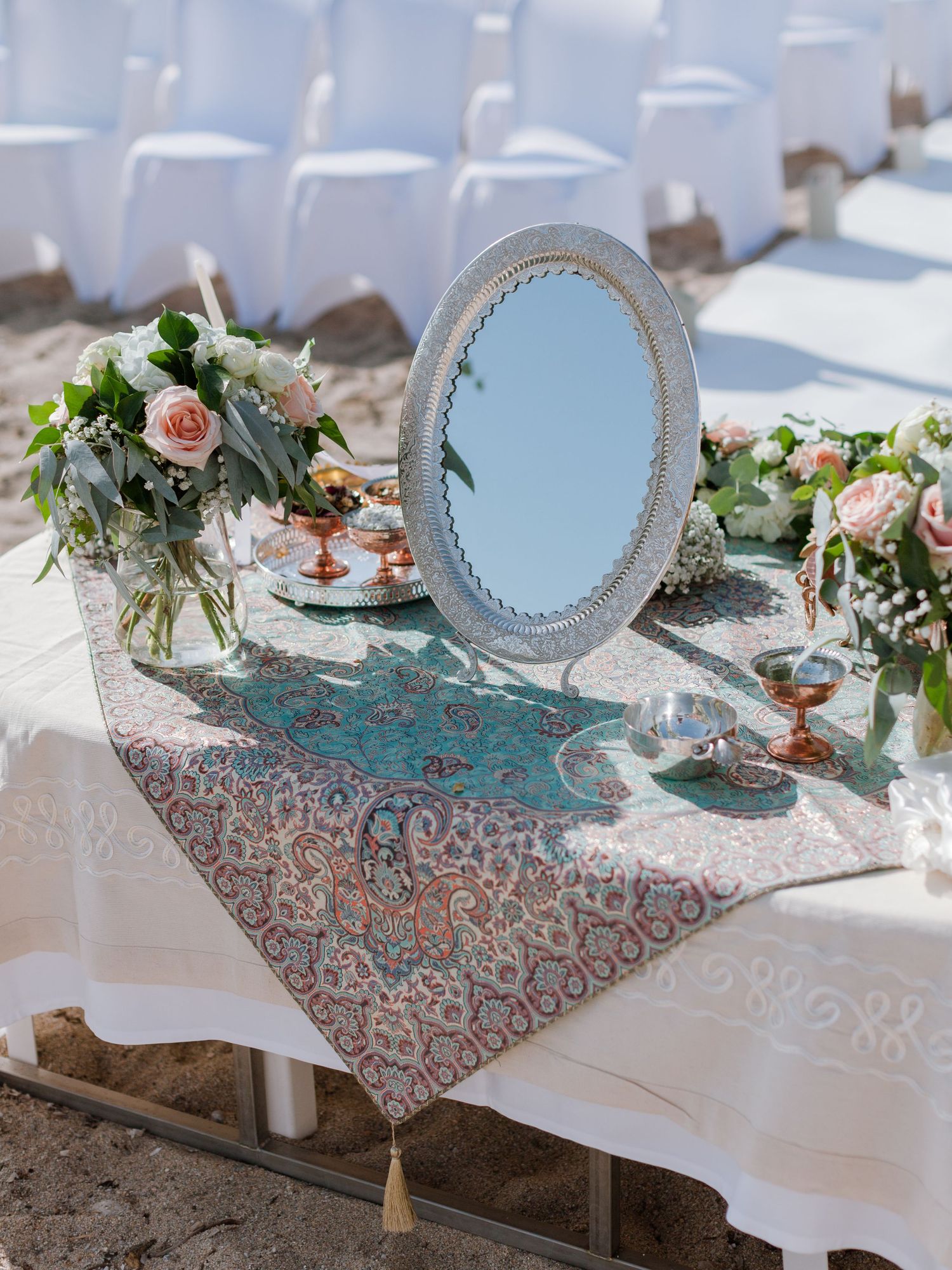 Élégante table de cérémonie de mariage persan (*sofreh aghd*) sur une plage de sable, ornée d'un miroir travaillé, de bouquets de roses