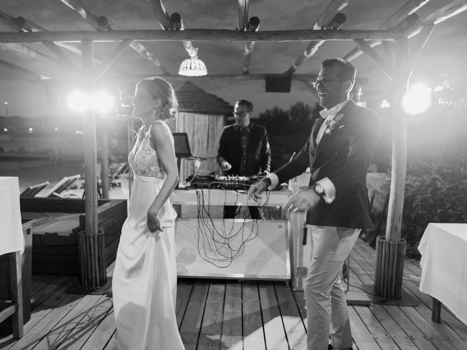 Photo en noir et blanc d'une mariée et d'un marié dansant à leur réception de mariage, avec un DJ en arrière-plan.