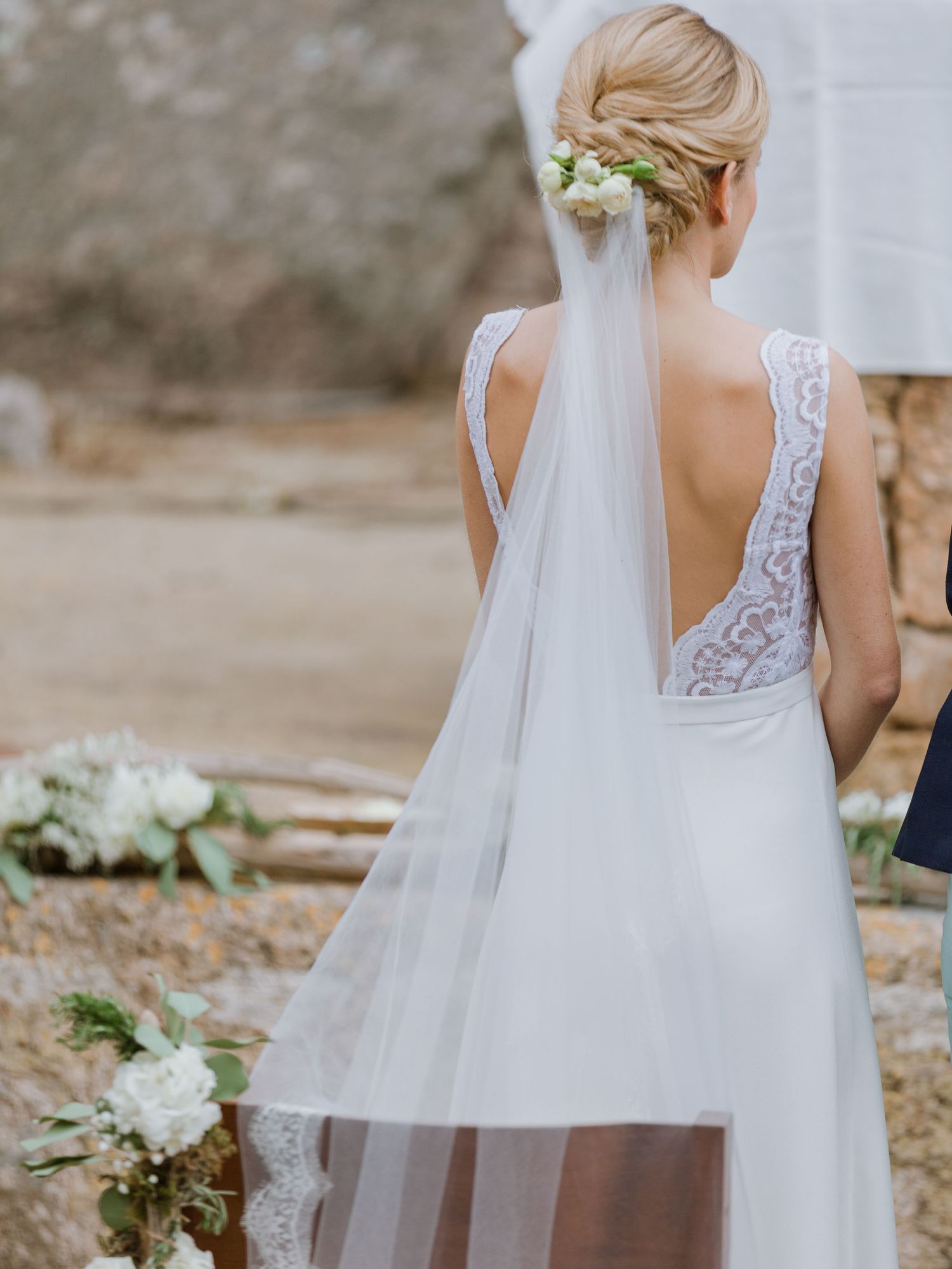 Mariée en robe de mariée élégante en dentelle dos nu, coiffée d'un chignon fleuri et portant un voile fluide, lors d'une cérémonie