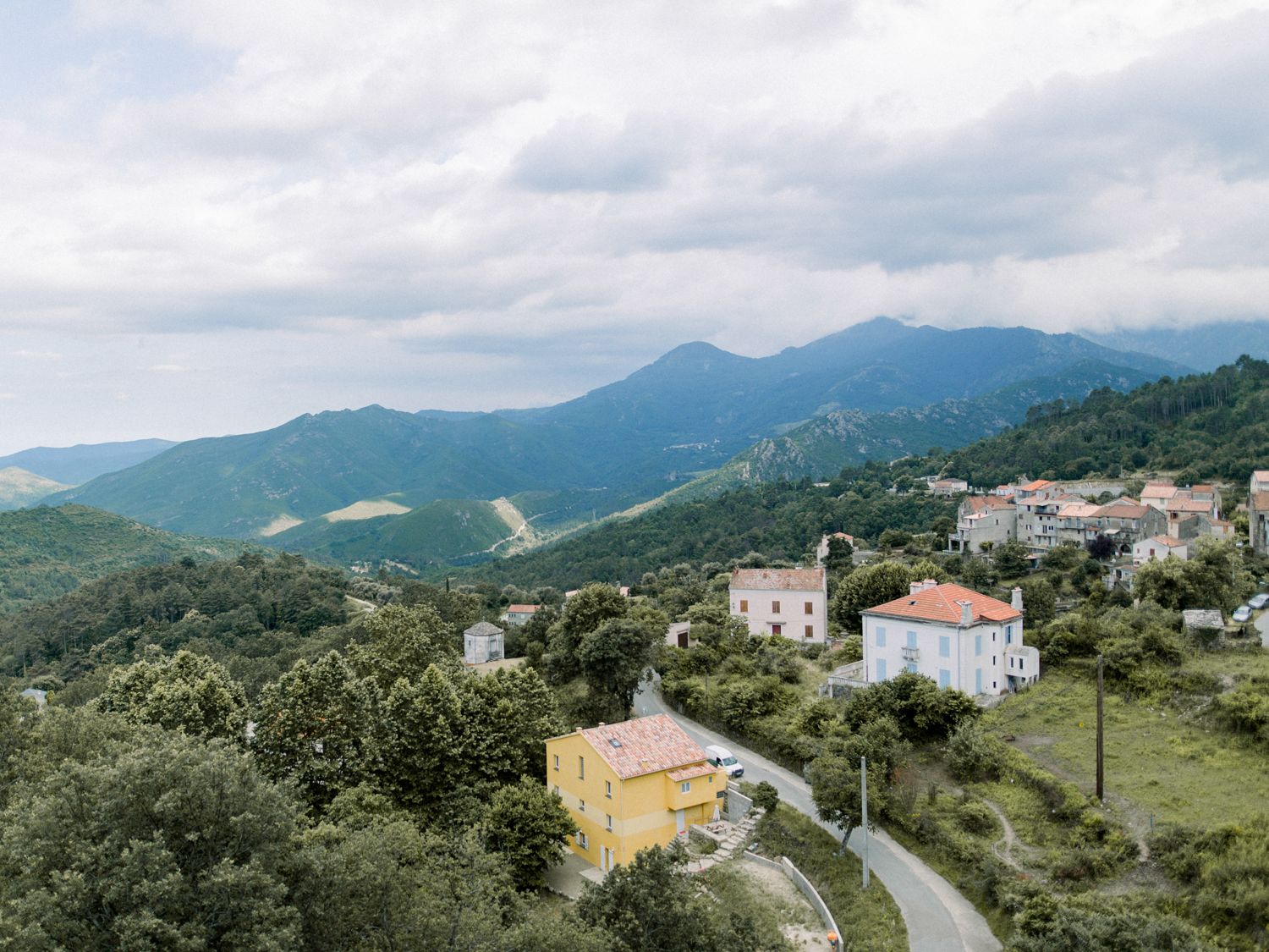 Aerial view of a small Italian mountain village surrounded by lush green hills and scenic mountain landscape.