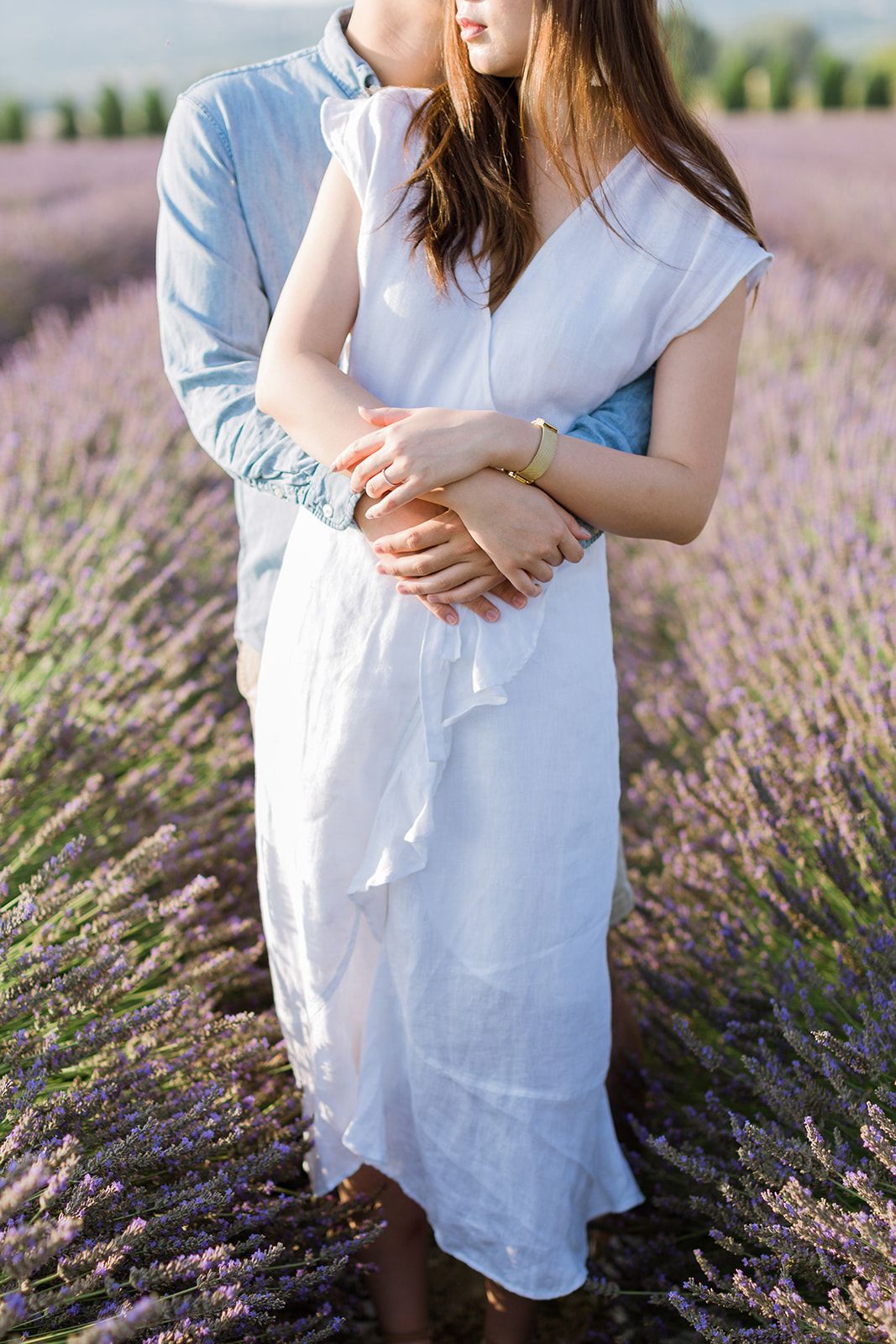 Un homme tenant une femme en robe blanche par derrière dans un champ de lavande en fleurs à Gordes en Provence.