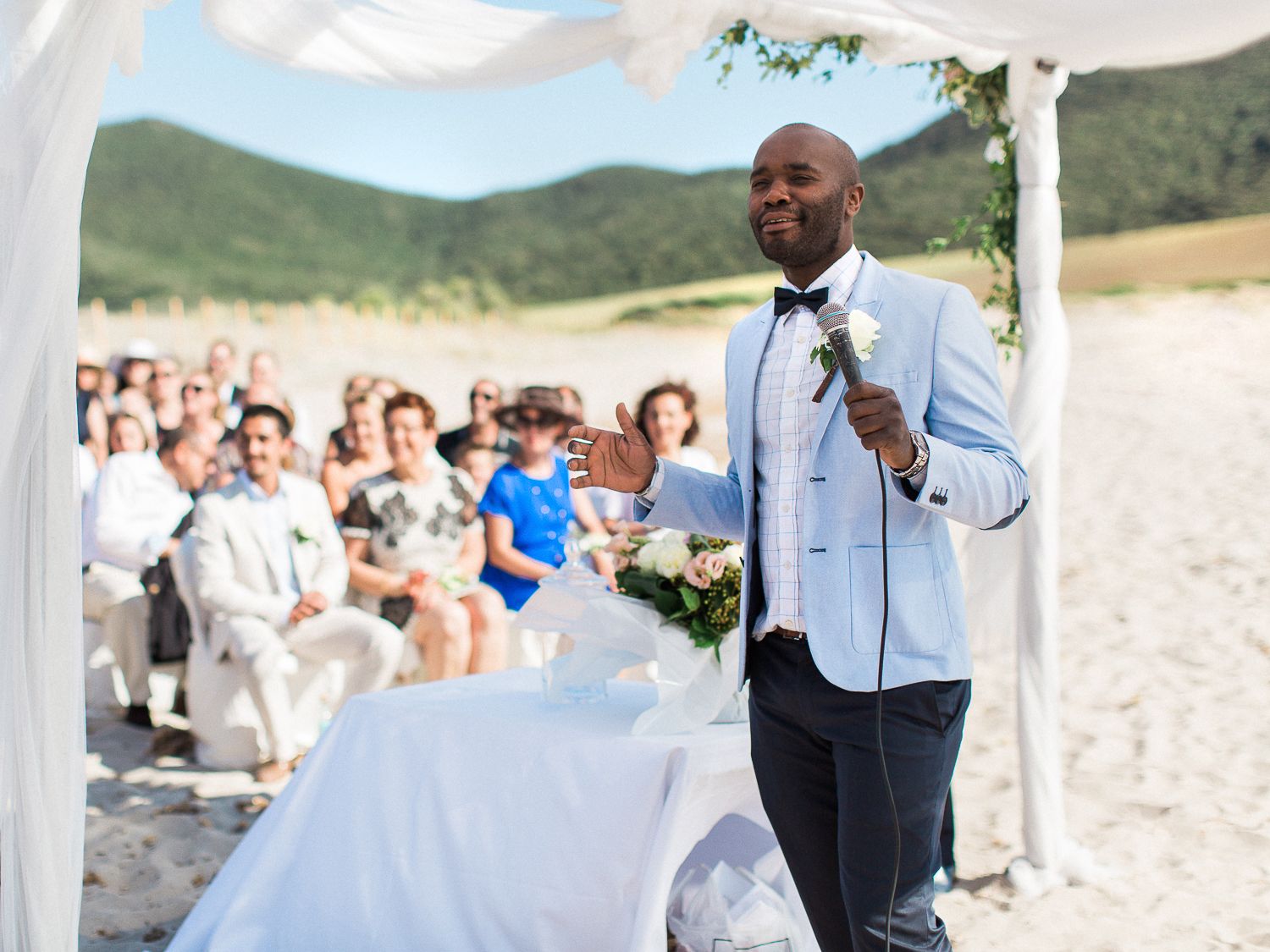 Le marié, vêtu d'un costume bleu clair, prend la parole lors de la cérémonie de mariage en plein air sur la plage