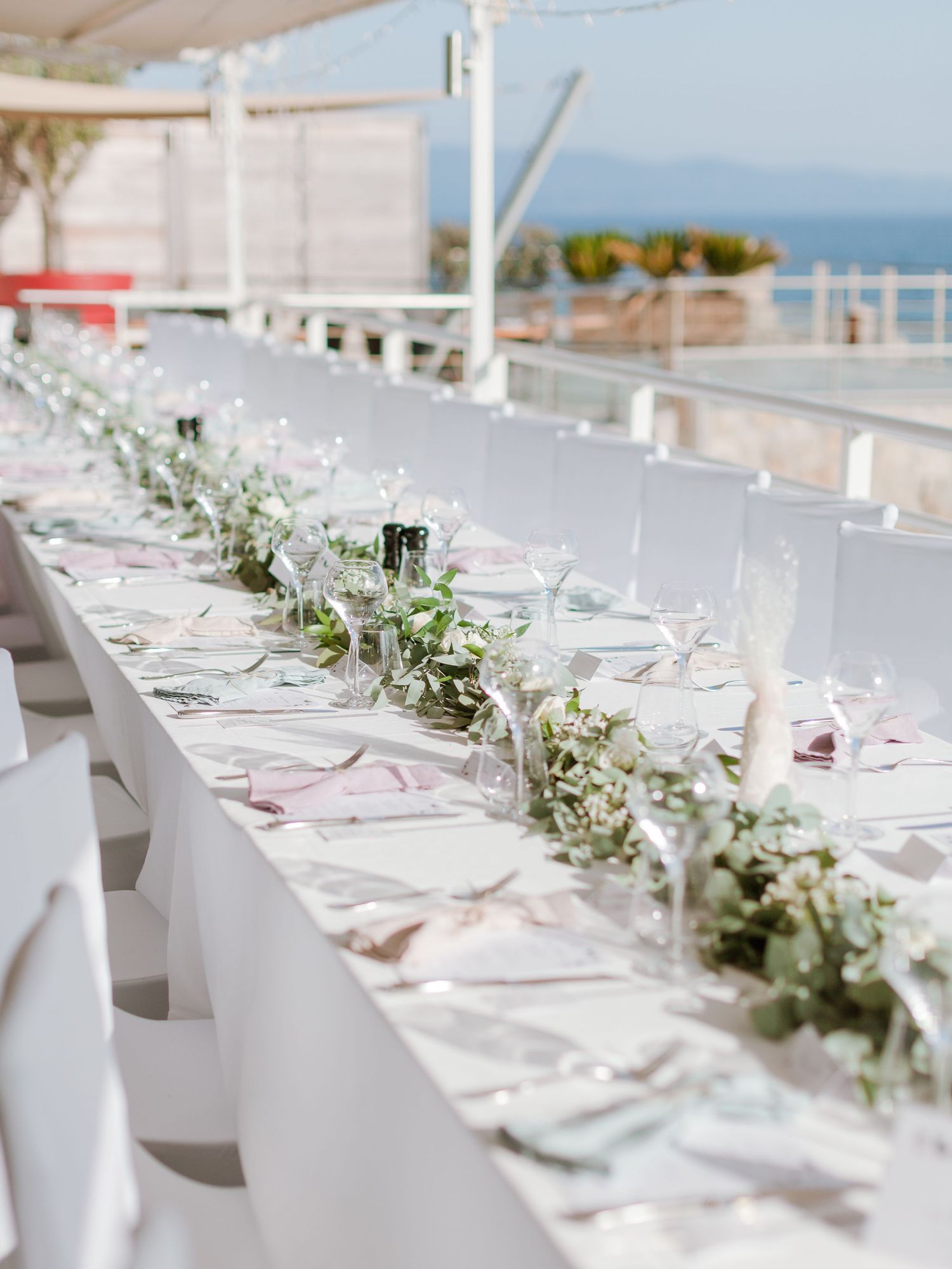 Table de réception de mariage en plein air élégante, agrémentée d'une guirlande de feuillage, de linge de table blanc et de verrerie