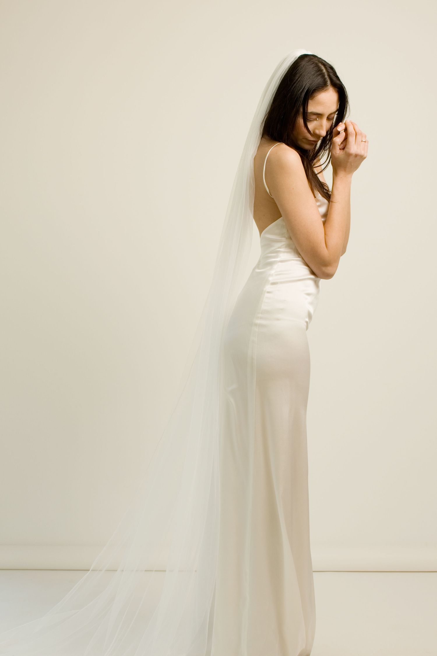 Une mariée en robe de satin ivoire et voile cathédrale, posant avec élégance sur un fond neutre by romance