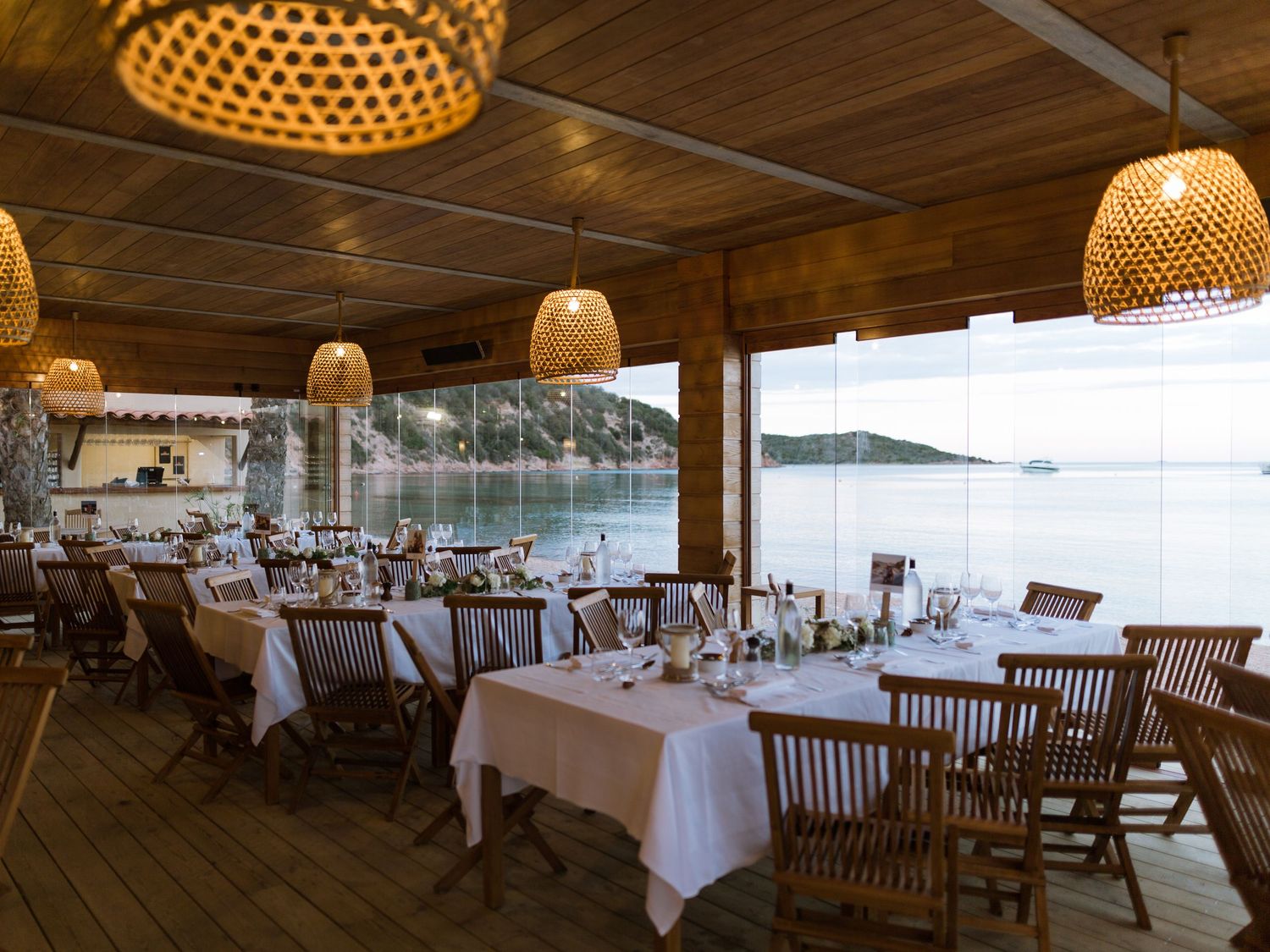 Restaurant élégant en bord de mer, avec nappes blanches, chaises en bois et suspensions lumineuses au maora Beach Bonifacio en corse