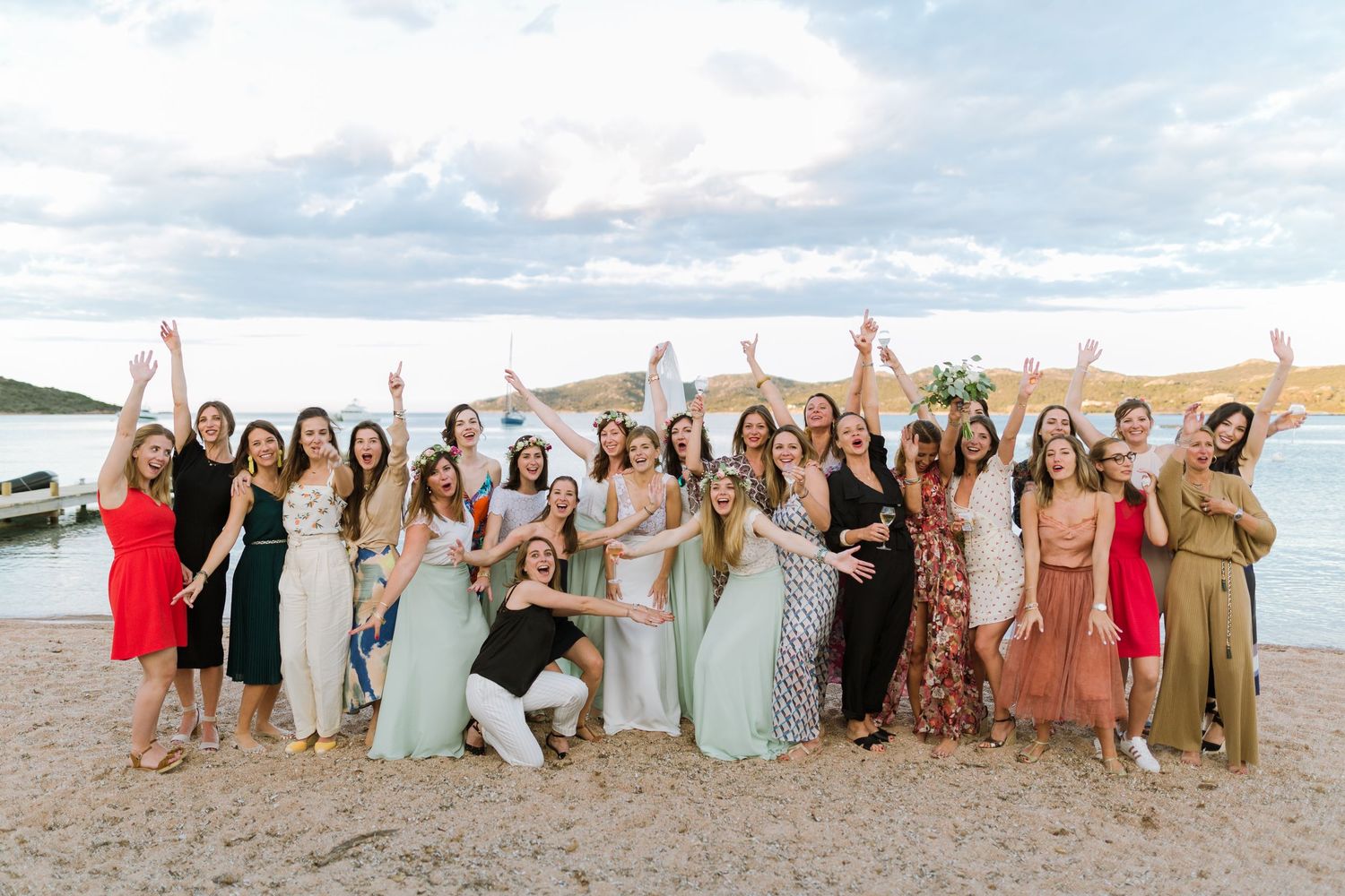 Un grand groupe de femmes célèbrent un mariage  en plein air sur une plage, levant joyeusement les mains. en corse au maora beach
