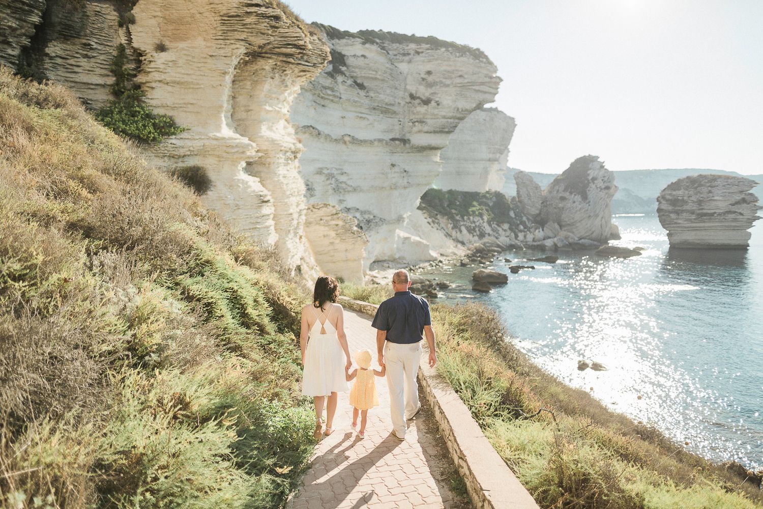 Promenade en famille le long d'un sentier côtier bordé de spectaculaires falaises de calcaire blanc et d'une mer bleue à Bonifacio.