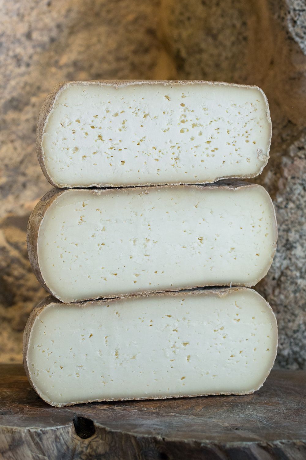 Trois moitiés de fromage de brebis corse à croûte naturelle, empilées sur une surface en bois rustique.