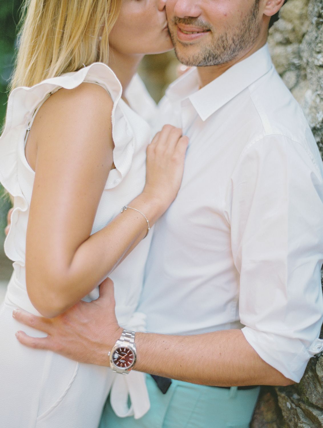 Un couple romantique s'embrasse en plein air, une femme en robe blanche à volants embrassant un homme en chemise blanche portant une montre