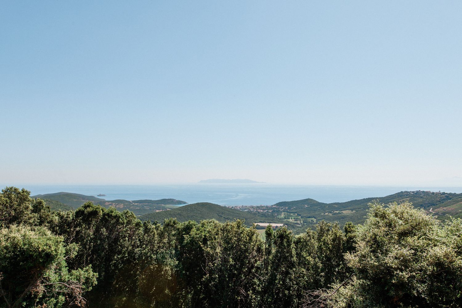 Panoramic view of lush green hills and mountains overlooking a calm blue sea under a clear sky.