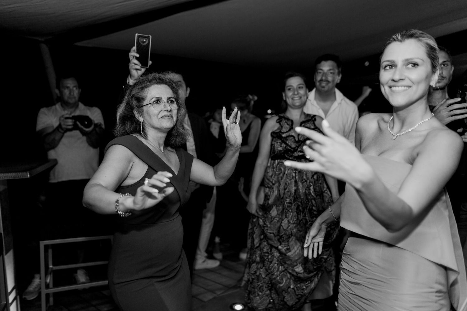 Des invités dansent et prennent des photos lors d'une réception de mariage animée ; photographie en noir et blanc.