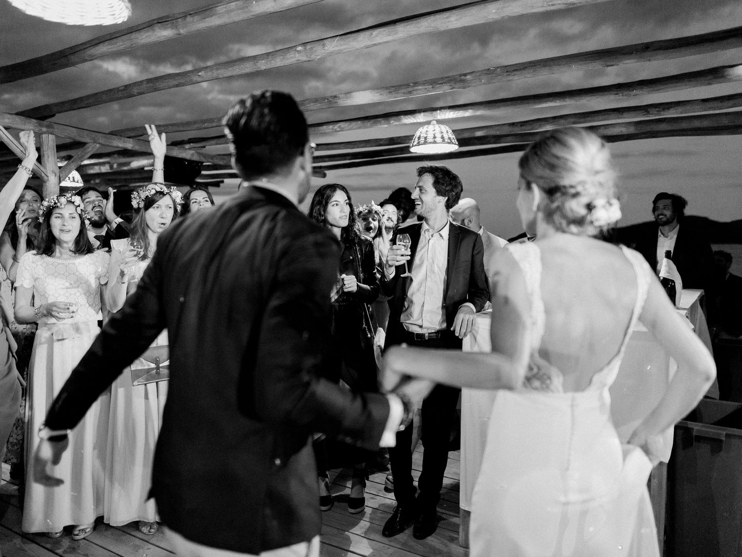 Photo de mariage en noir et blanc des mariés dansant avec les invités en arrière-plan. Au maora Beach Bonifacio en corse