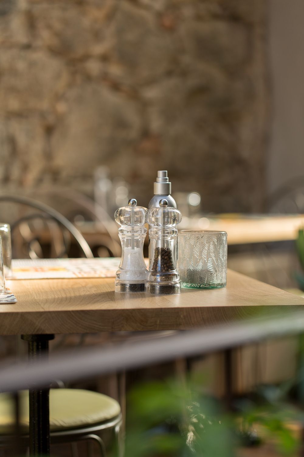Moulins à sel et à poivre avec un verre sur une table de restaurant en bois, devant un mur en pierre.