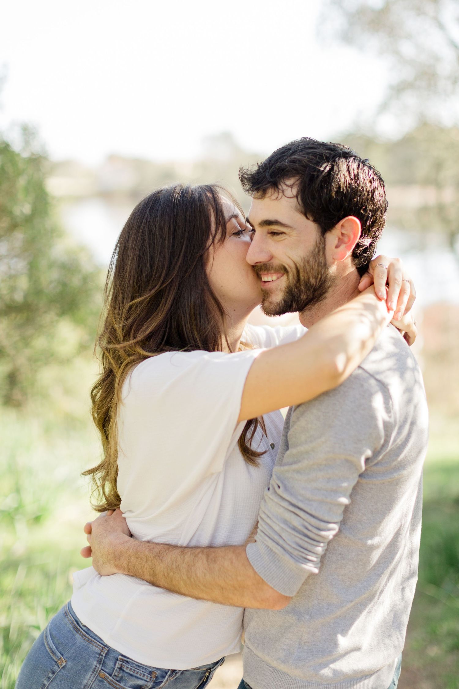 Un couple heureux s'embrasse en plein air, baigné par la lumière naturelle du soleil, avec de la verdure en arrière-plan.