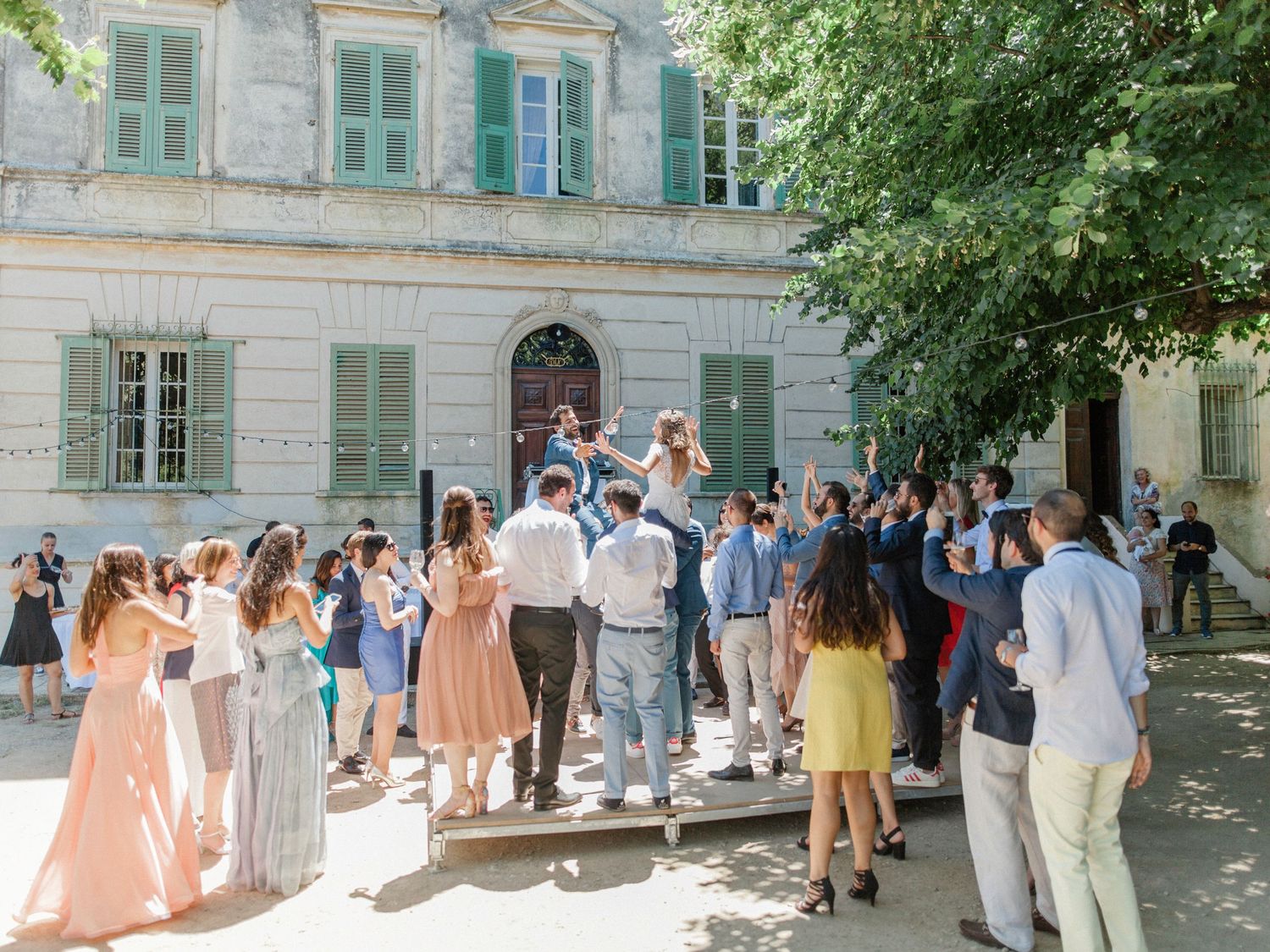 Elegant outdoor wedding celebration with guests gathered in front of a classic French manor on a sunny day.