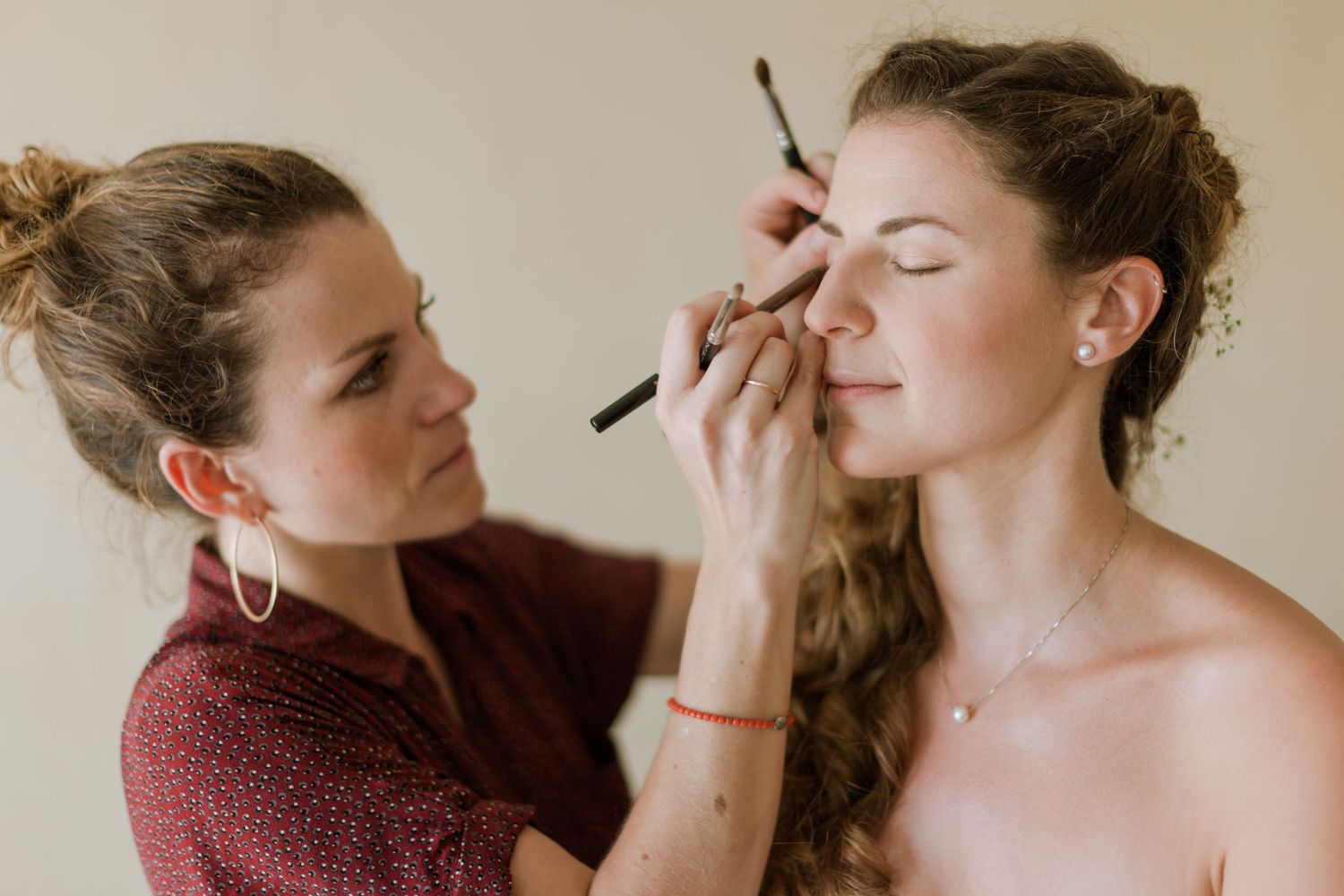 Maquilleuse professionnelle appliquant du maquillage des yeux à une mariée aux cheveux bouclés avant sa cérémonie de mariage.