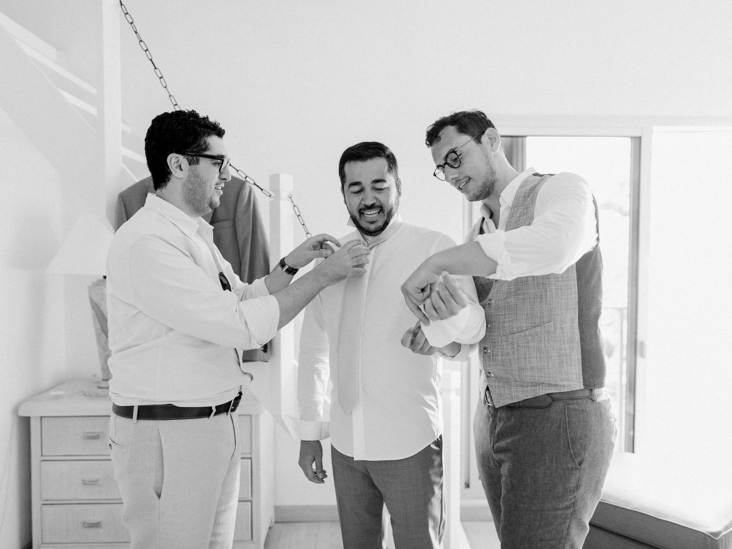 Garçons d'honneur aidant le marié à s'habiller avant la cérémonie de mariage, sur une photo en noir et blanc.
