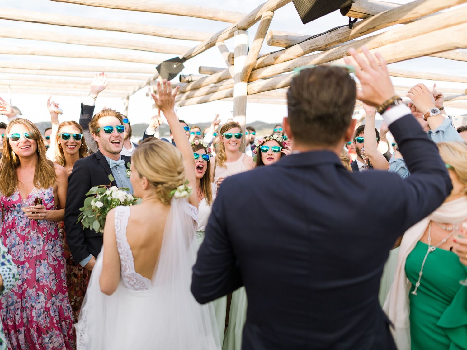 Les jeunes mariés sont célébrés par leurs invités, lunettes de soleil sur le nez, sous une pergola en bois lors d'une réception