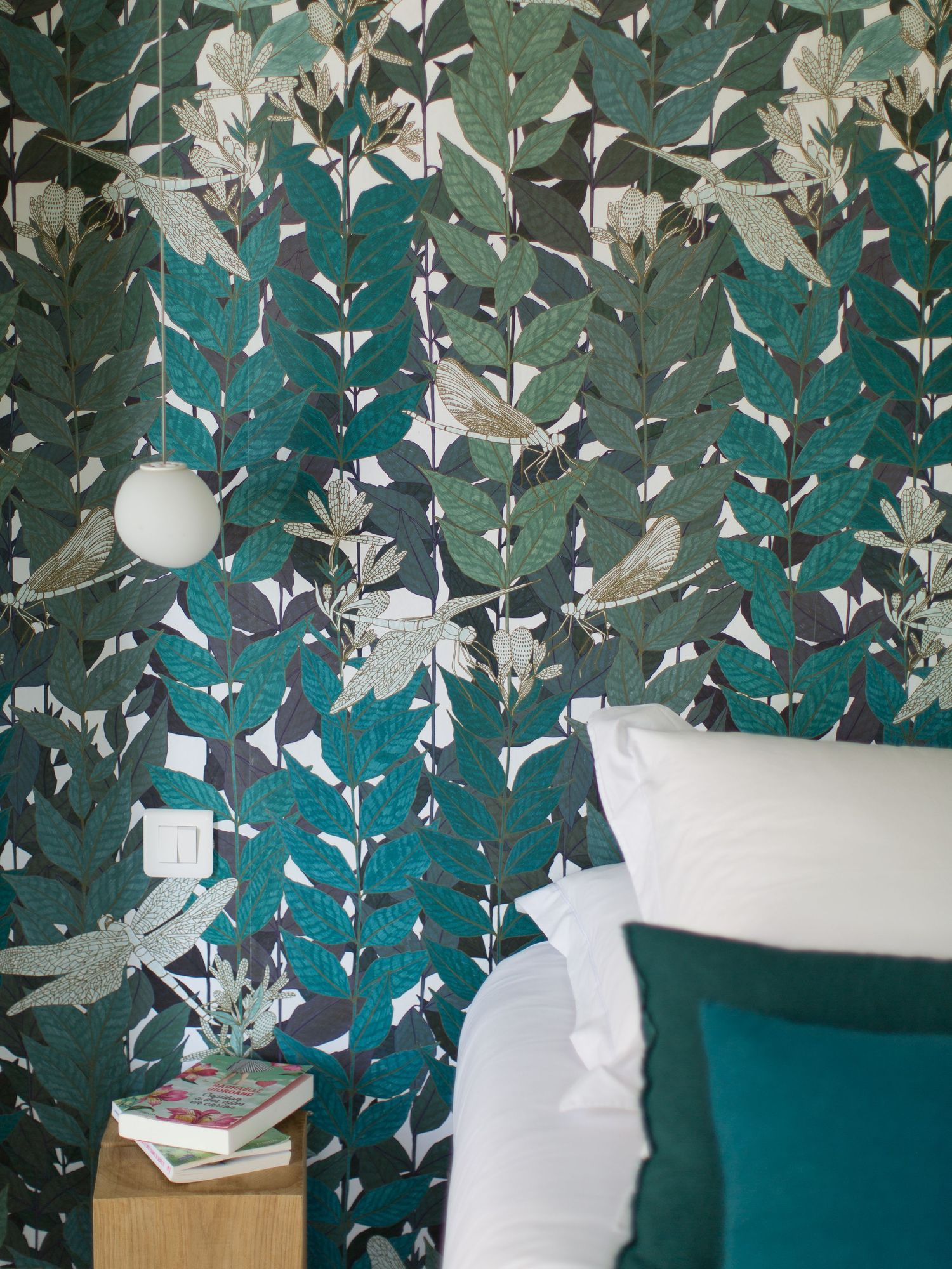 Mur de chambre orné d'un papier peint à motifs de feuilles tropicales audacieuses, dans des tons turquoise, et rehaussé de coussins blancs.