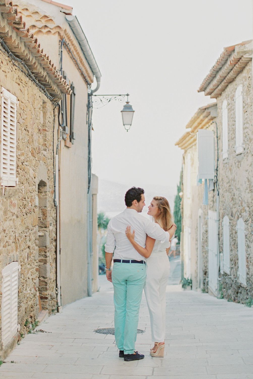 Un couple s'enlace et manque de s'embrasser dans une charmante ruelle pavée d'un village français.