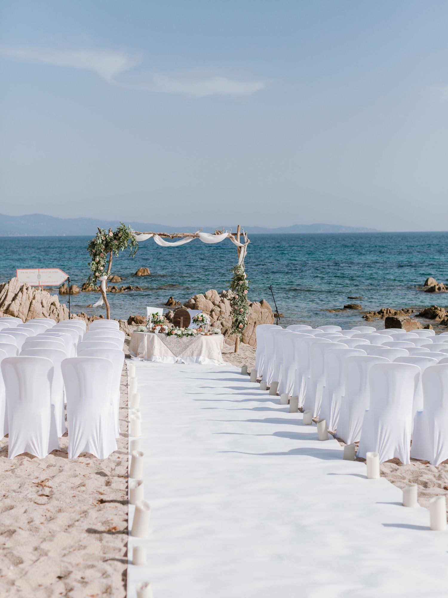 Installation élégante pour une cérémonie de mariage en bord de mer, avec des chaises blanches et une arche florale