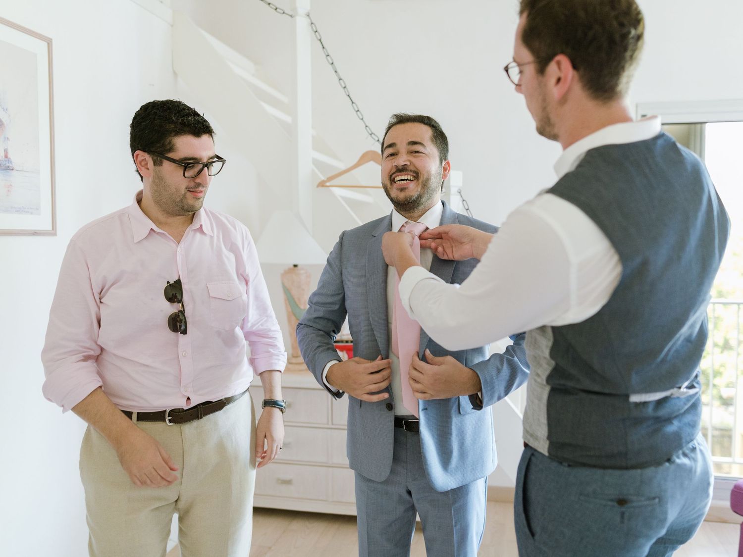 Trois hommes en tenue habillée aident un futur marié à ajuster sa cravate alors qu'il se prépare pour la cérémonie de mariage.
