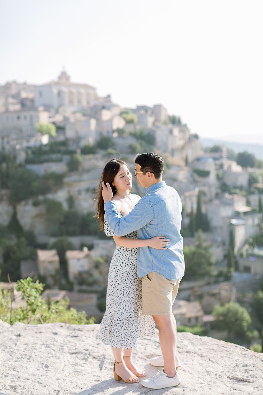 Un couple partage un moment d'intimité sur une falaise rocheuse, avec le magnifique village perché de Gordes, en France, en arrière-plan.