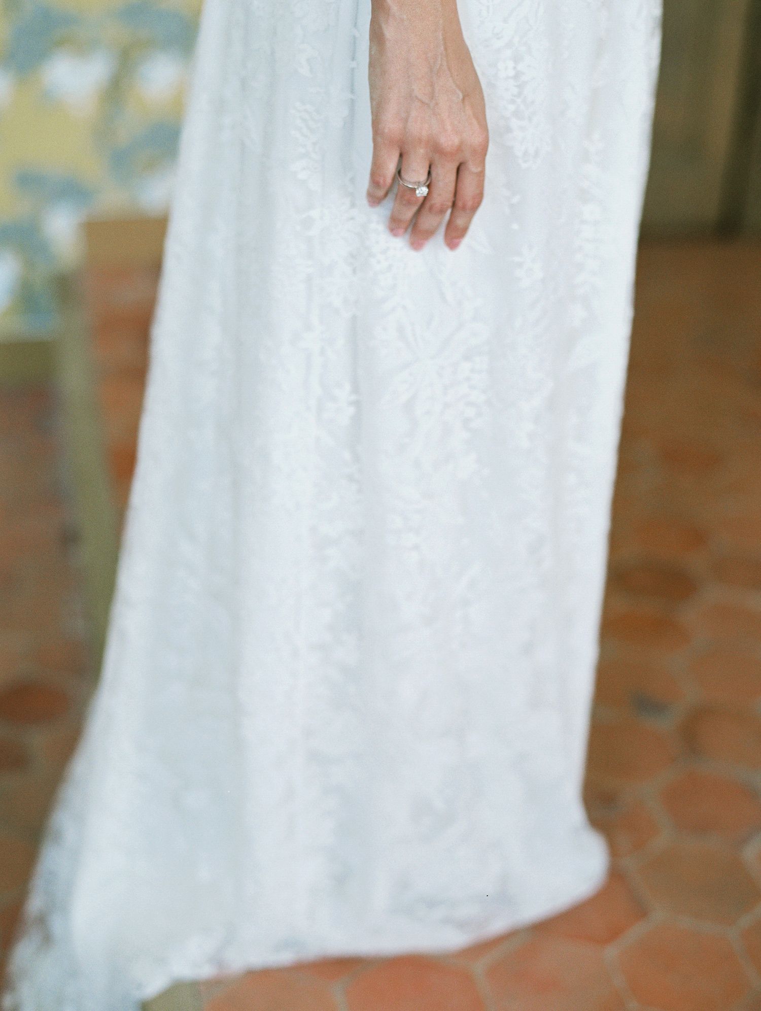 Close-up of a bride in a white lace wedding gown, wearing a diamond ring on her finger.
