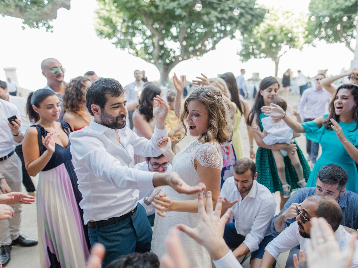 Bride and groom dancing joyfully with wedding guests outdoors at a lively reception celebration.