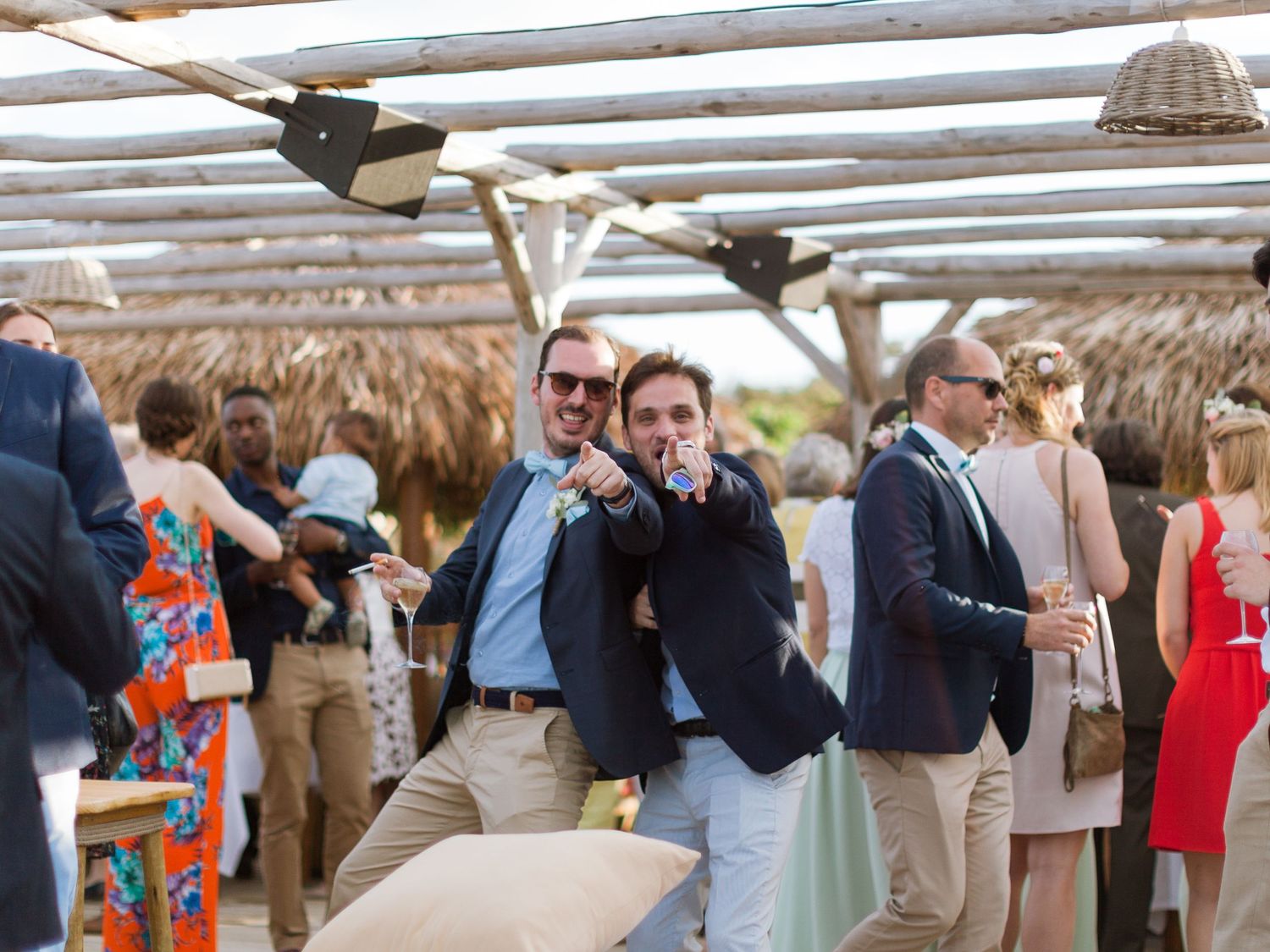 Deux hommes en blazers posent et pointent du doigt l'objectif lors d'une réception de mariage en plein air sur la plage