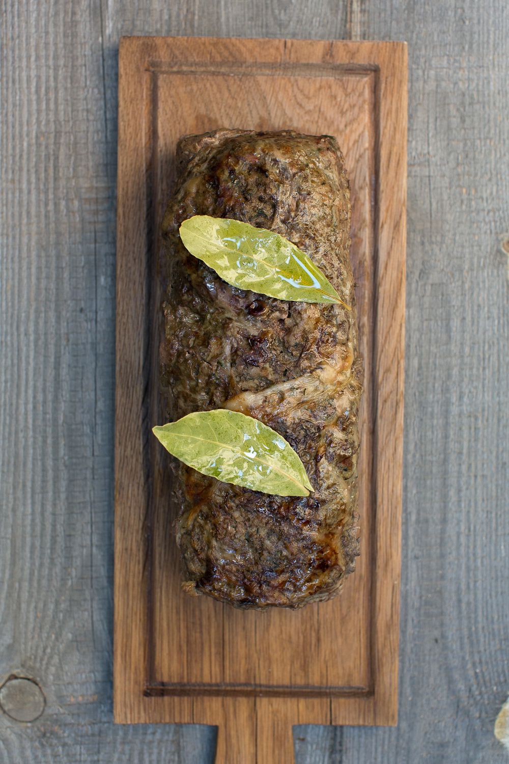 Pain de viande rustique garni de feuilles de laurier, servi sur une planche à découper rectangulaire en bois à L'orriu restaurant
