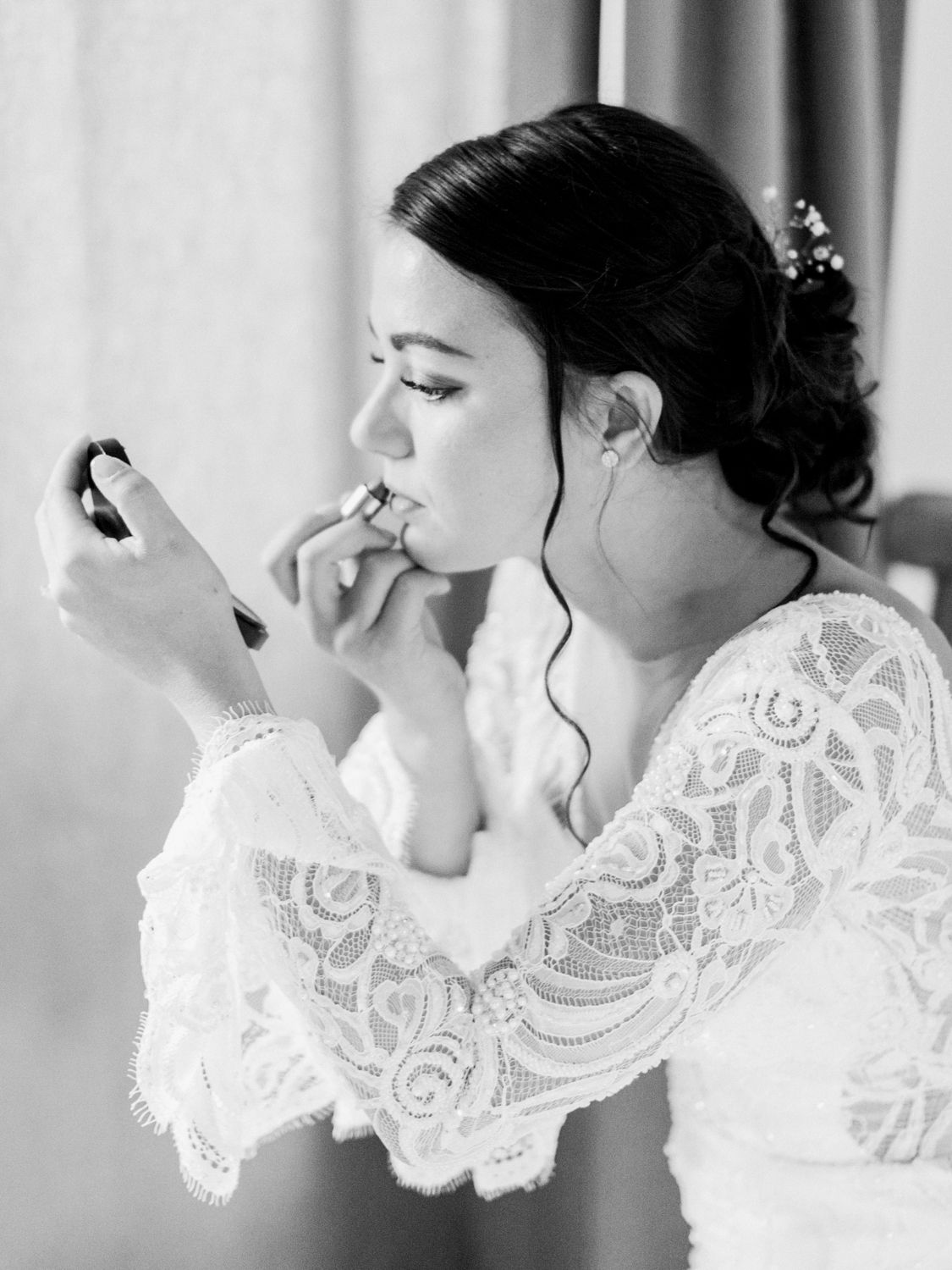 Une mariée se maquille en tenant un miroir de poche, vêtue d'une robe de mariée en dentelle blanche à Bandol Côte d'Azur.