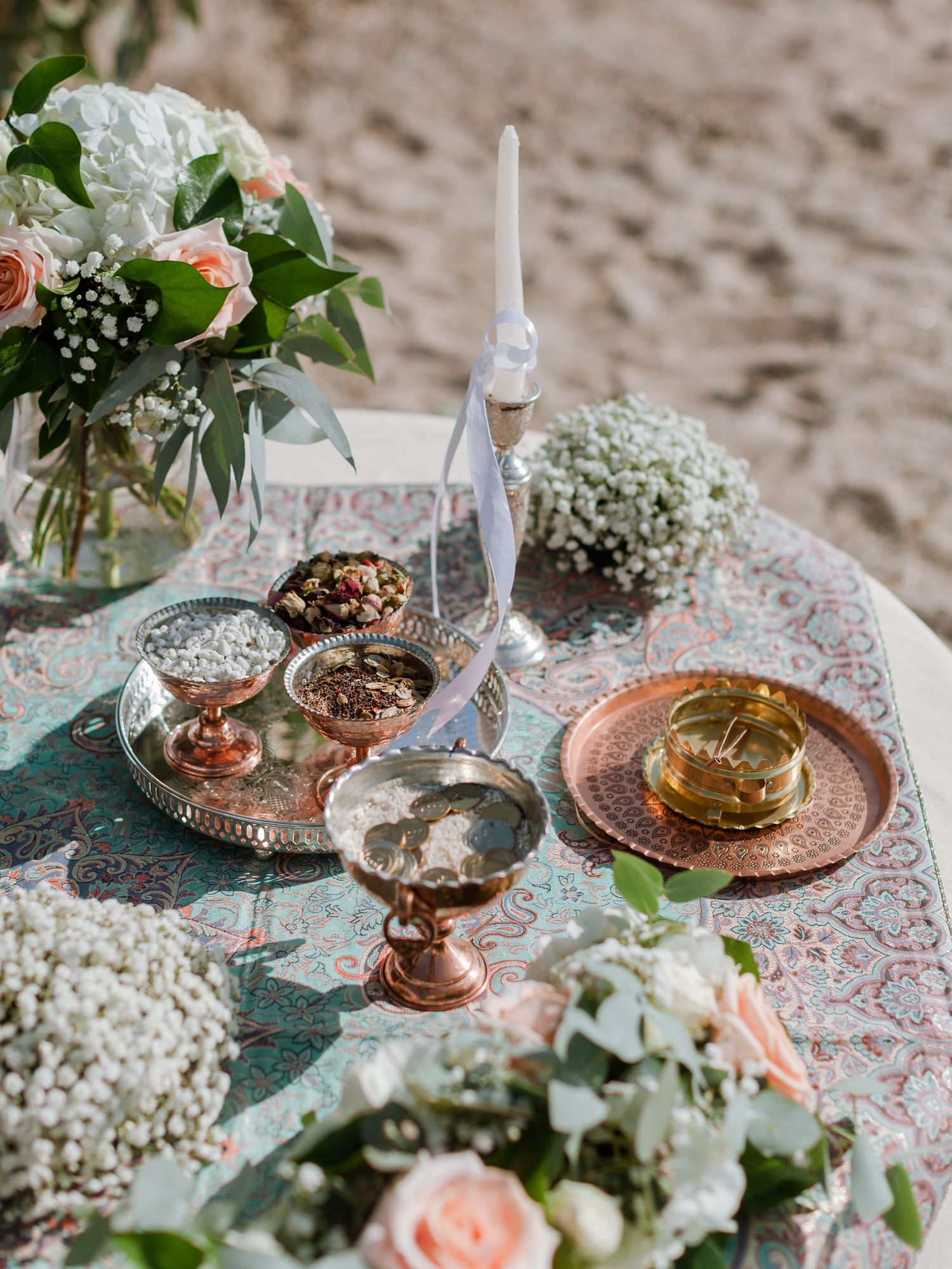 Table élégante pour un mariage à la plage, agrémentée de compositions florales, de récipients en cuivre, de bougies et de coupelles