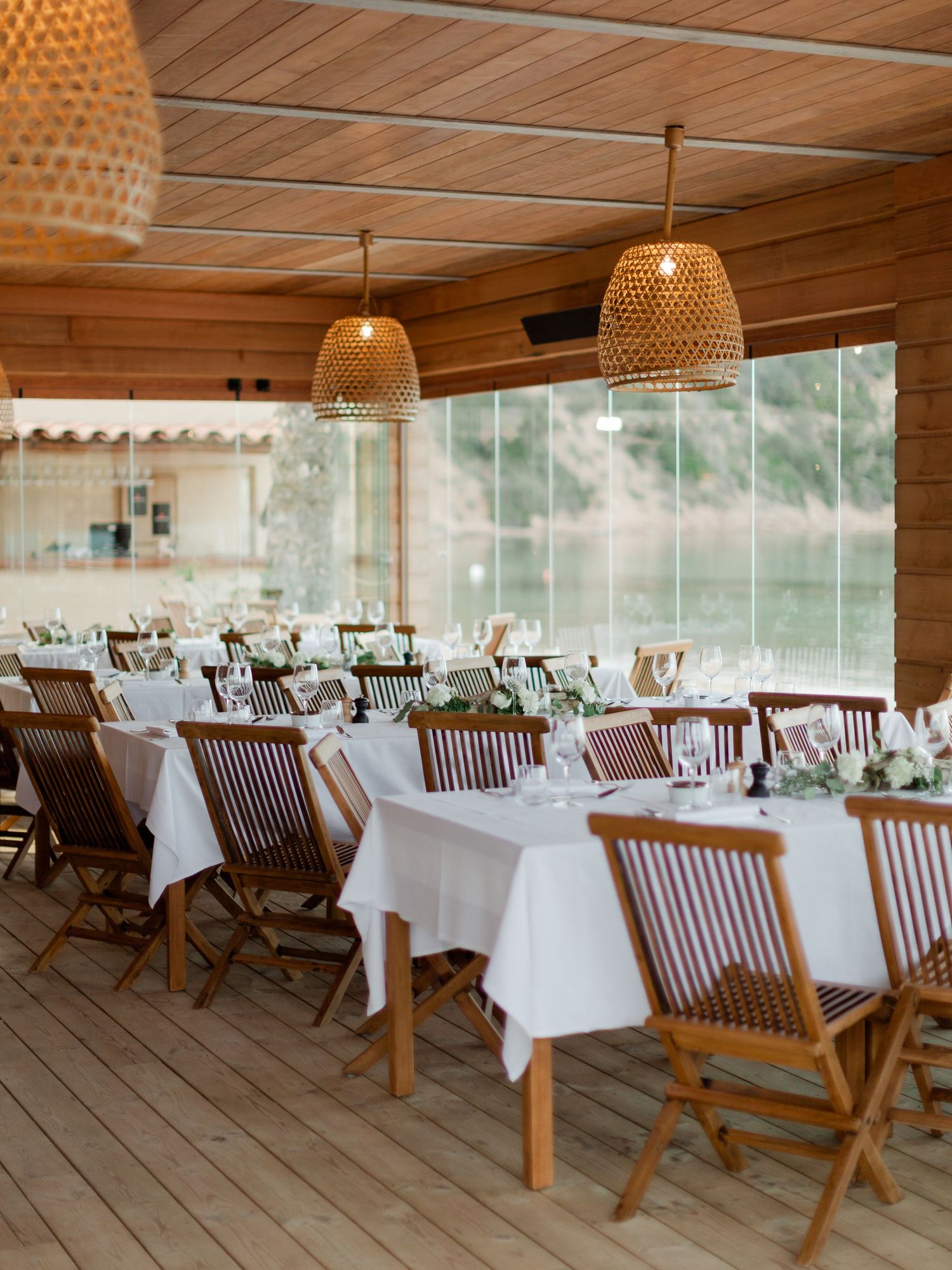 Salle à manger élégante d'un restaurant en bord de mer, avec chaises en bois, nappes blanches, suspensions lumineuses en osier