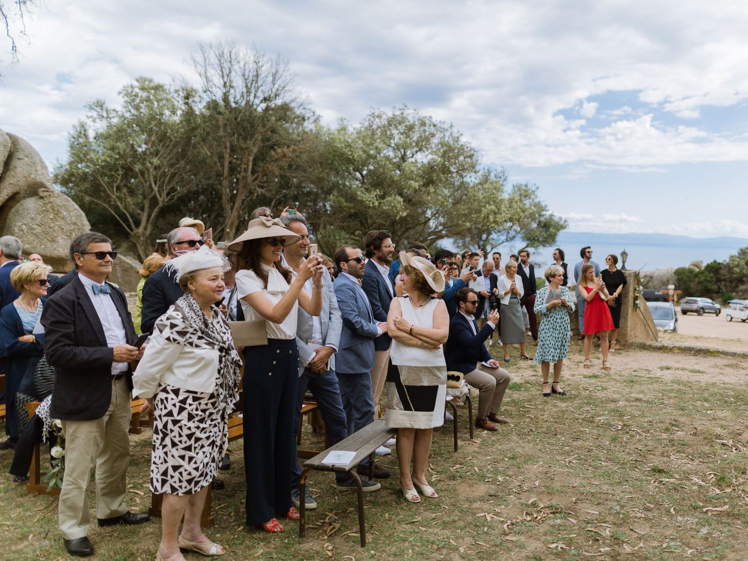 Les invités d'un mariage en plein air se sont réunis par une journée ensoleillée, vêtus de tenues de cérémonie et de chapeaux, avec les mont