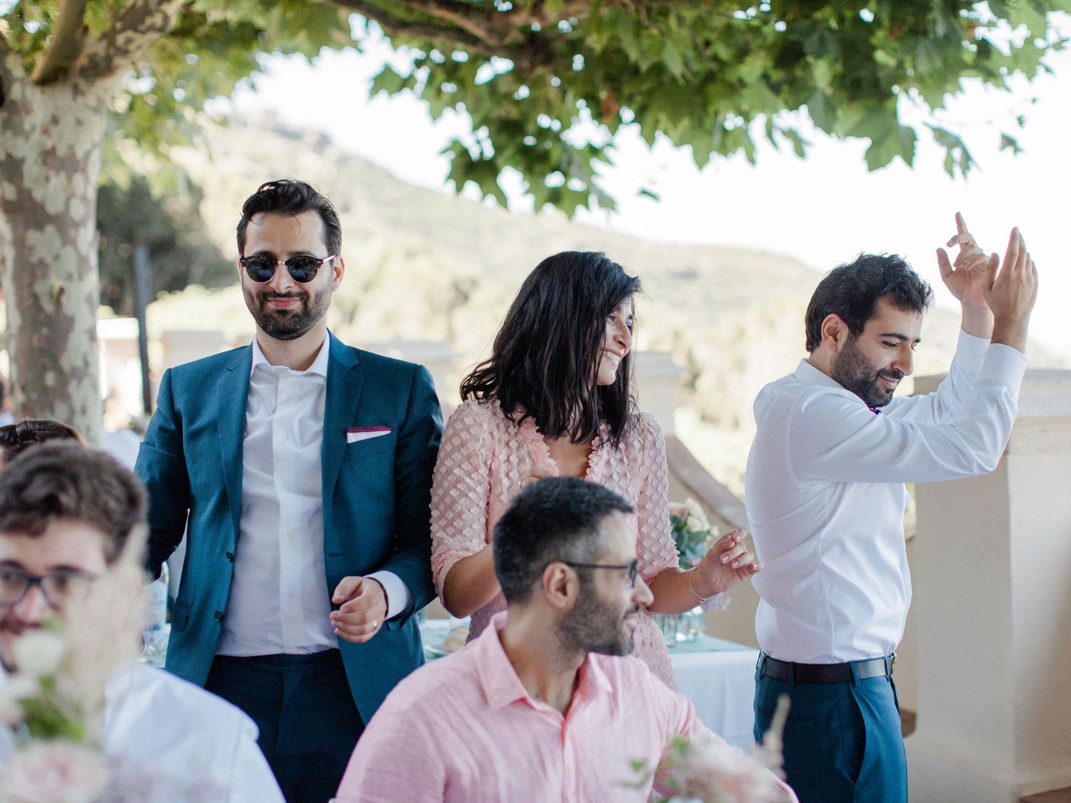 Guests laughing and dancing at an outdoor wedding reception on a sunny day.