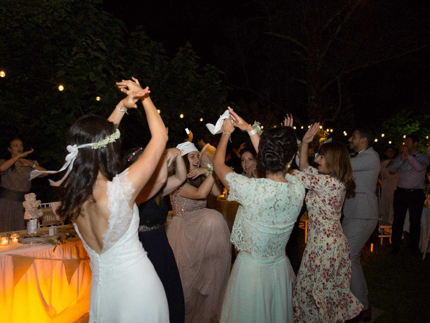 Des invités dansent joyeusement lors d'une réception de mariage en plein air, sous des guirlandes lumineuses.