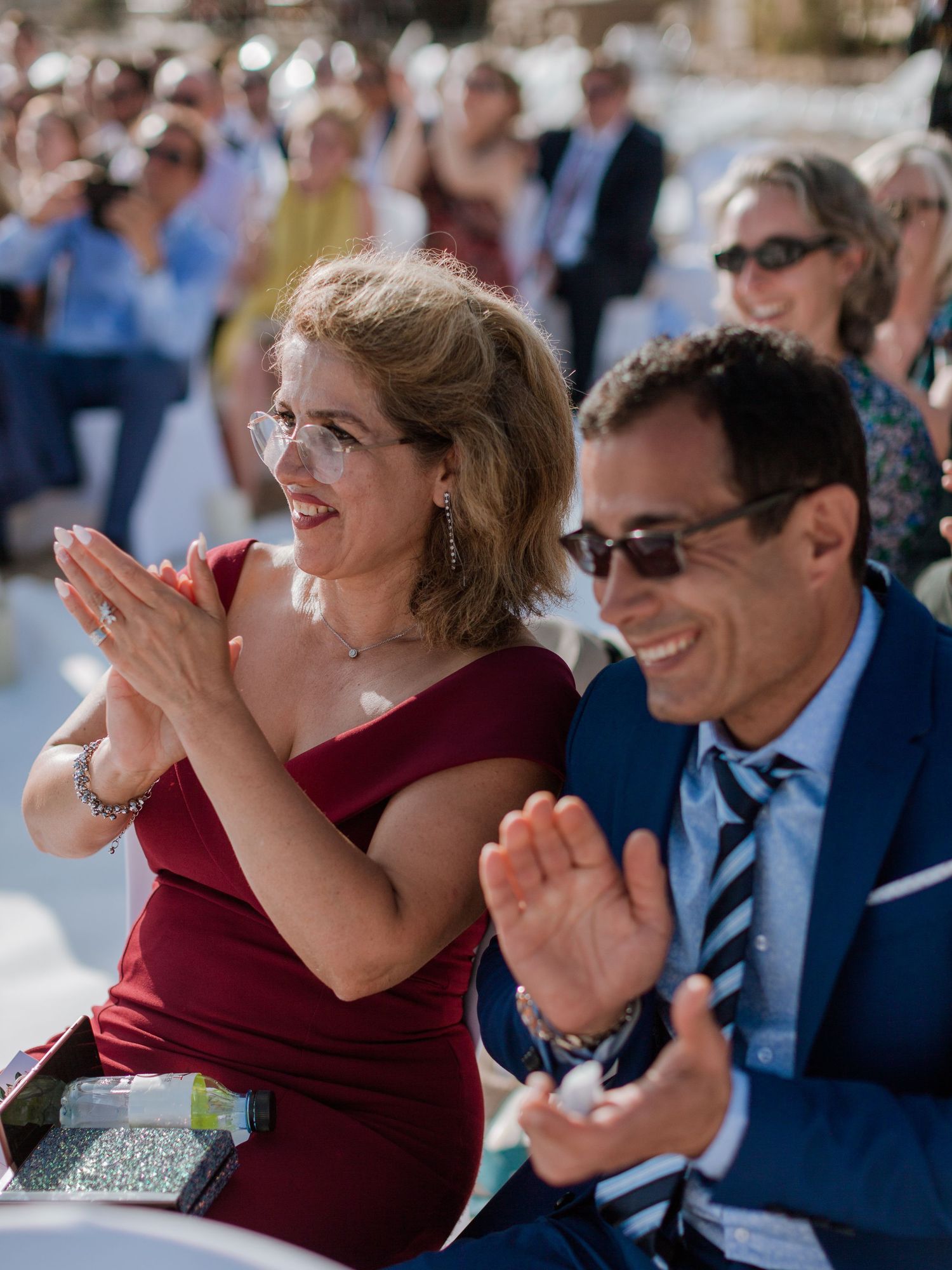 Des invités de mariage en tenue de cérémonie applaudissent et sourient lors d'une célébration en plein air.
